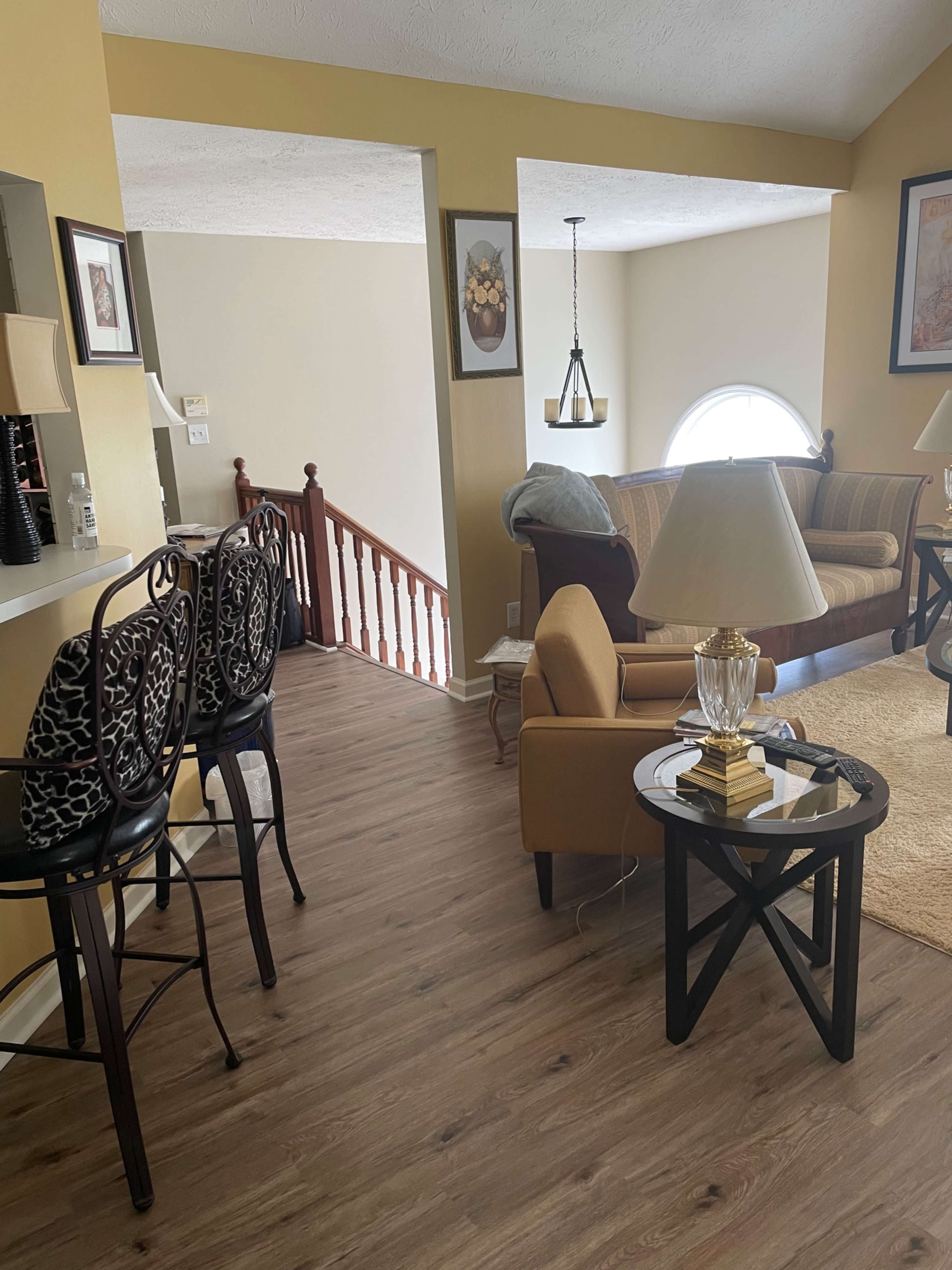 A living area with a sofa, a coffee table, and a staircase leading to an upper level, surrounded by yellow walls and framed artwork.