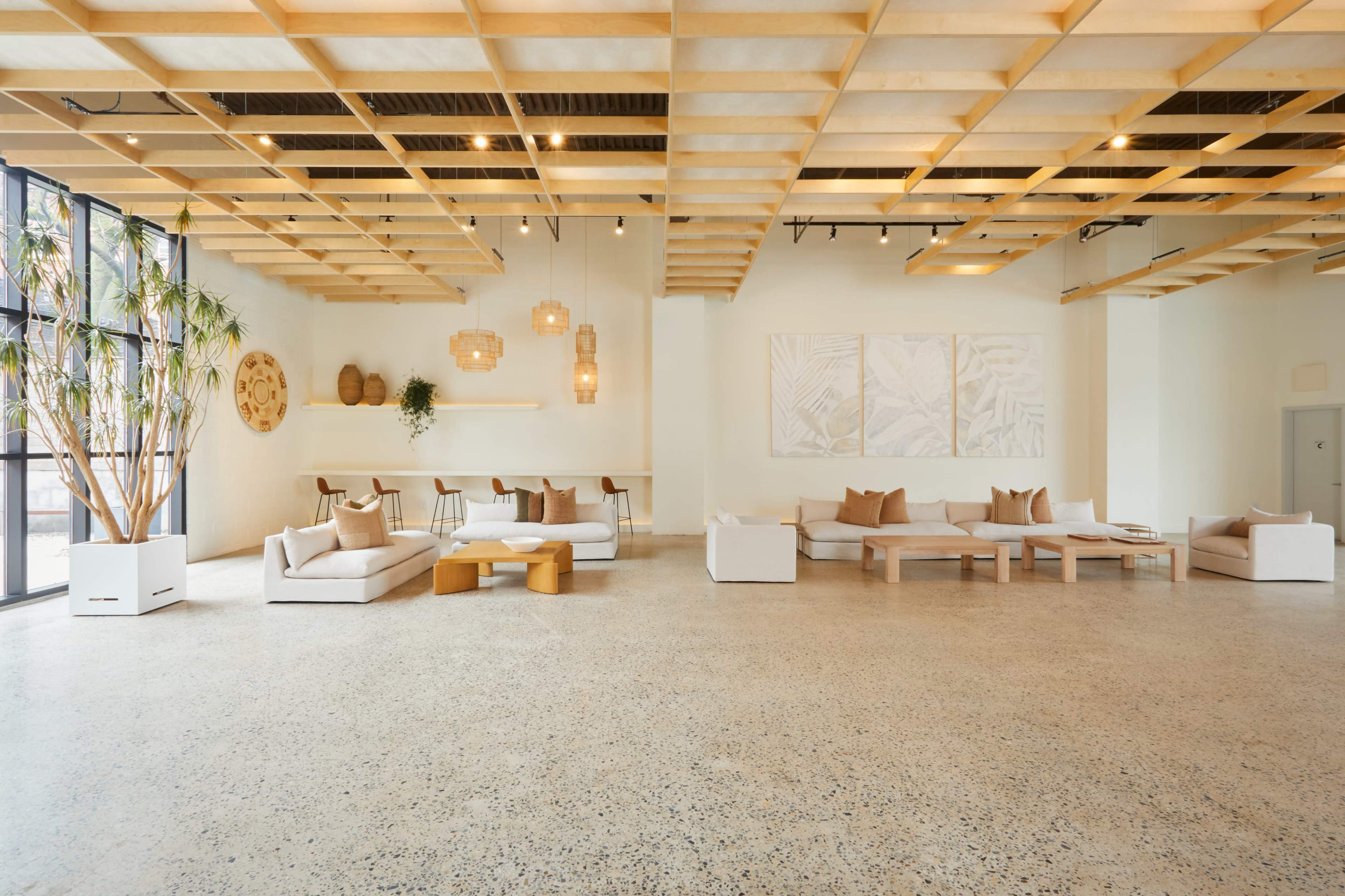 The image shows a spacious, modern interior with a polished concrete floor, wooden ceiling beams, and comfortable seating arrangements.