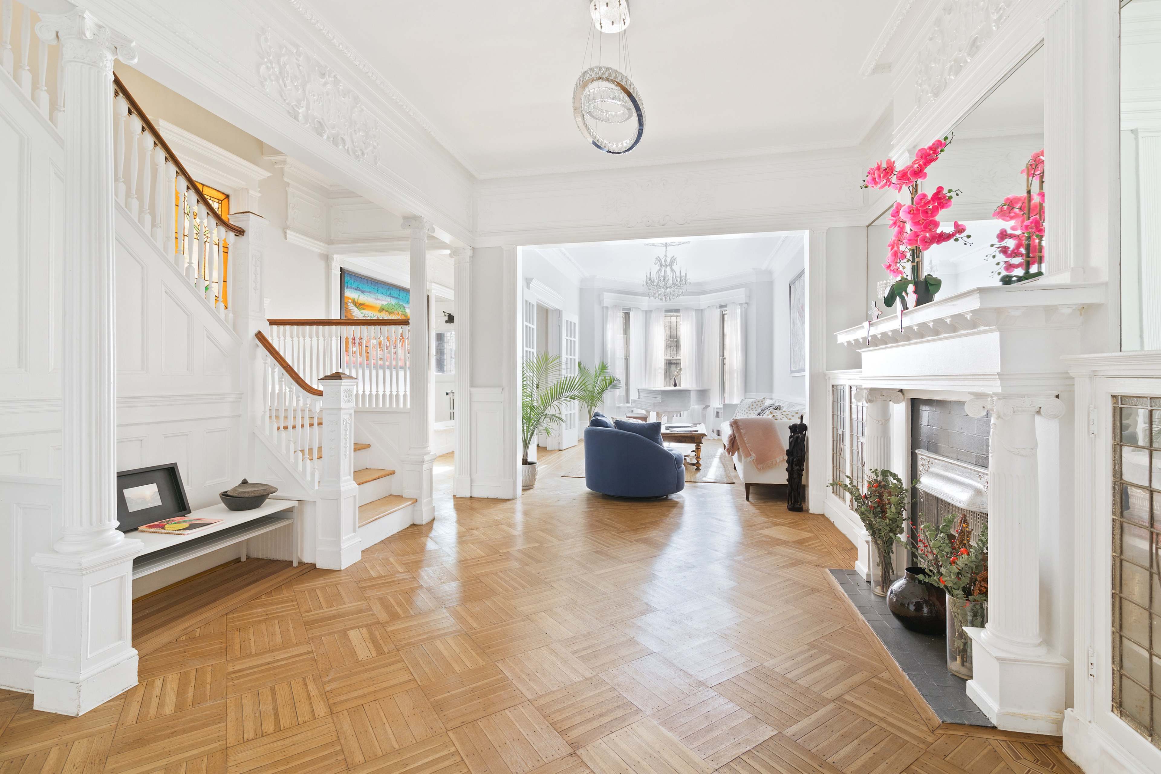 A bright, airy entrance hall leading to a living area with a staircase on the left and elegant furnishings visible in the background.