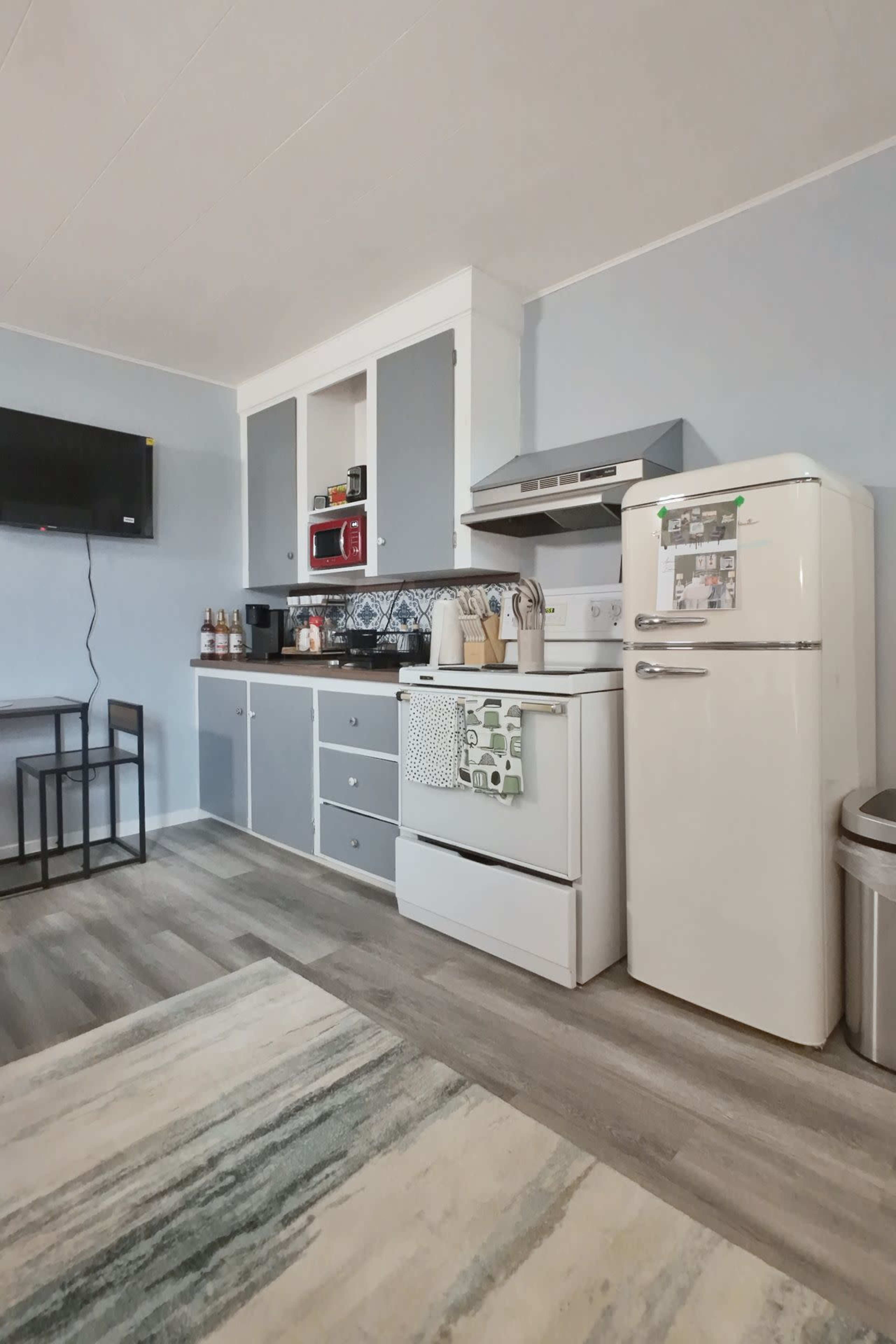 The image shows a modern kitchen with gray cabinetry, a white stove, a refrigerator, and a small dining table.