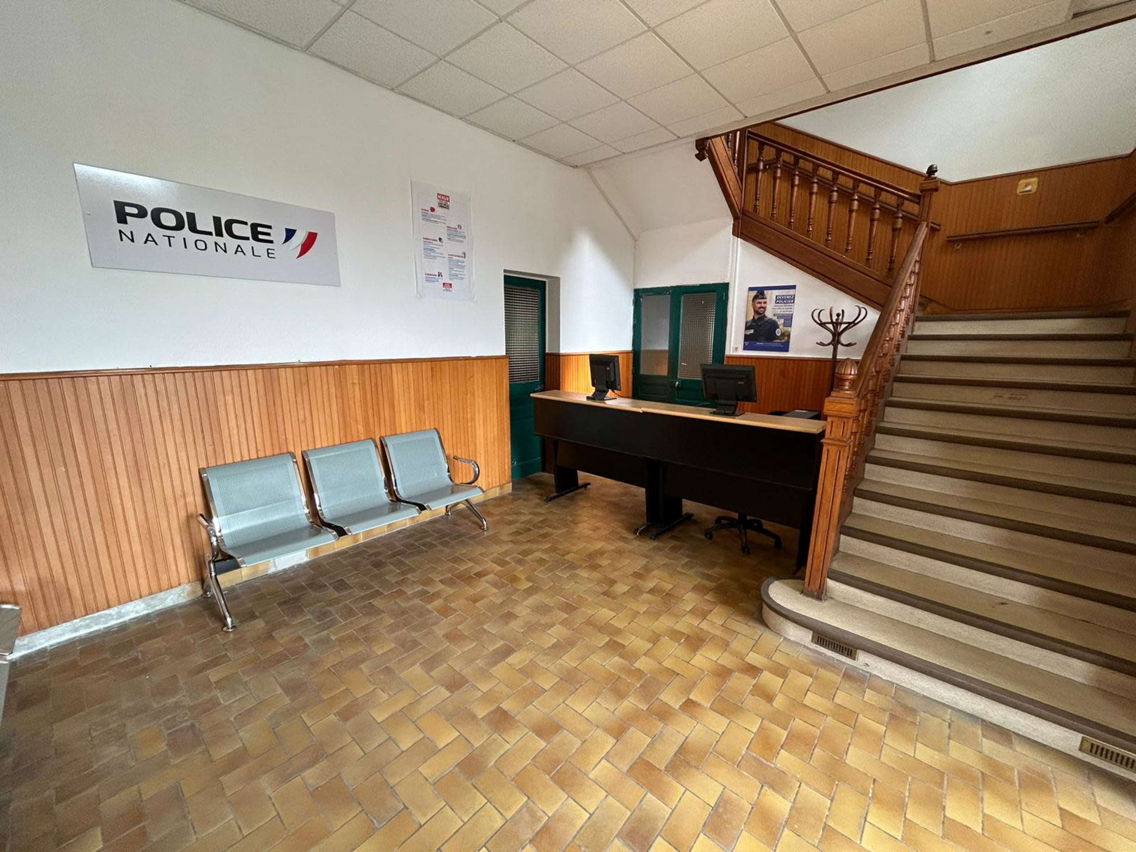 A waiting area in a police station featuring metal chairs, a reception desk, and a staircase.