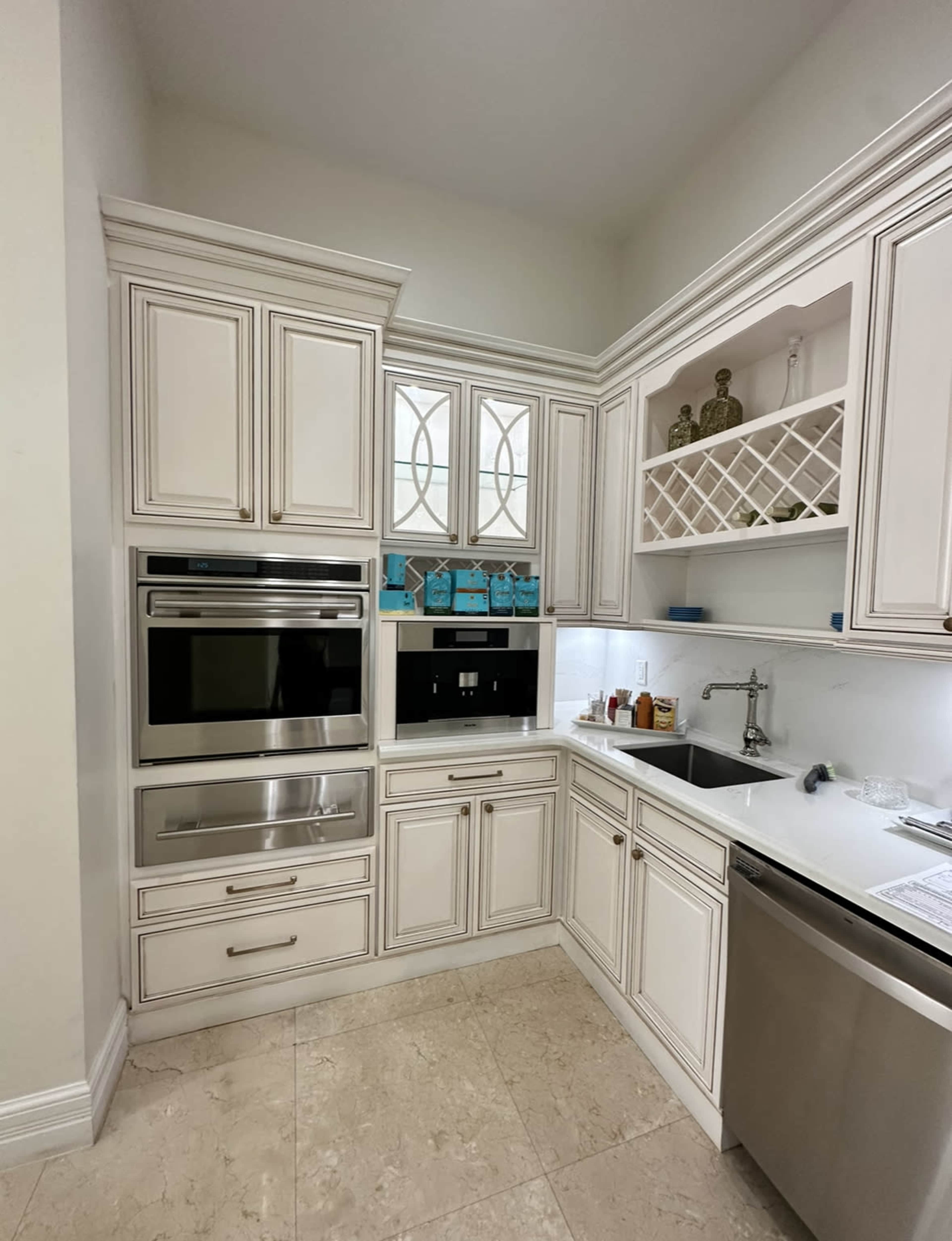 A modern kitchen with white cabinetry, built-in appliances, and a marble-tiled floor.