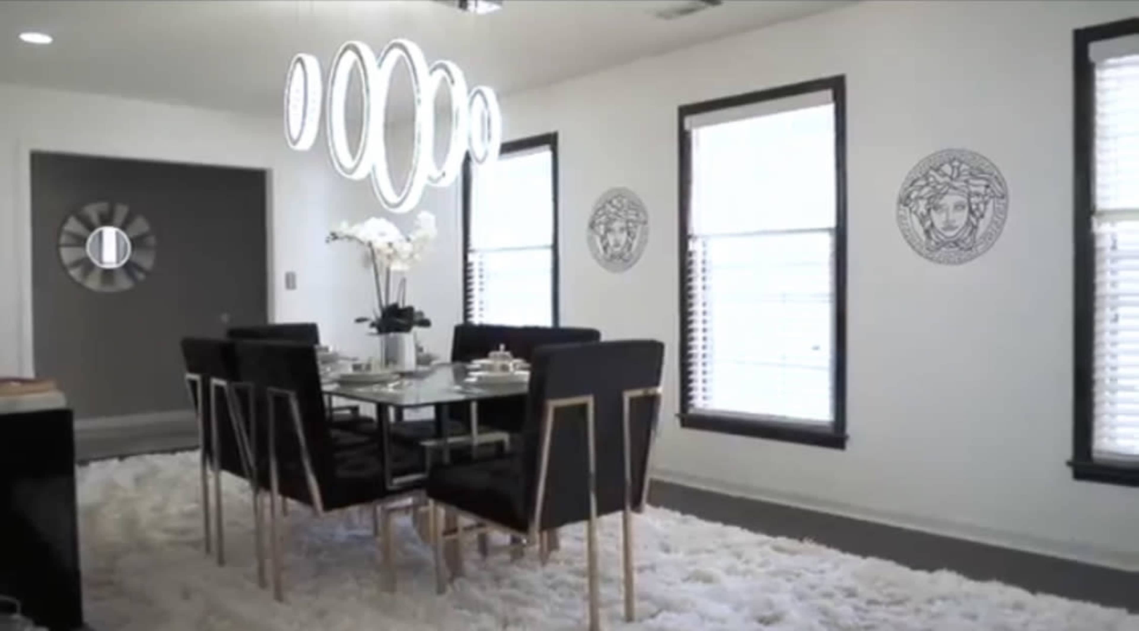 A modern dining room with a black and silver table set, surrounded by six black chairs, and illuminated by a circular pendant light, all atop a white rug.