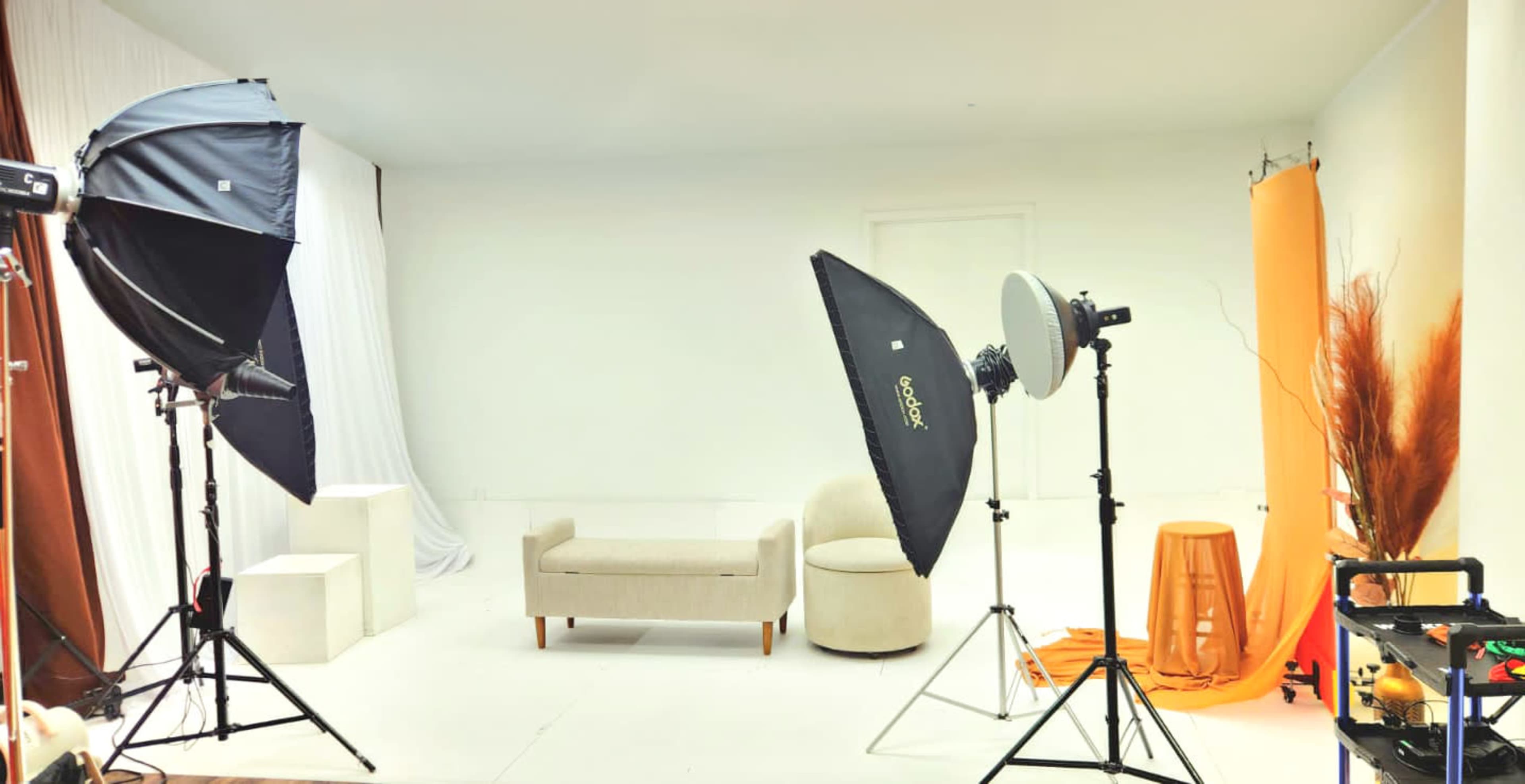 A photography studio is set up with two lighting softboxes, a gray backdrop, various props, and a beige couch.