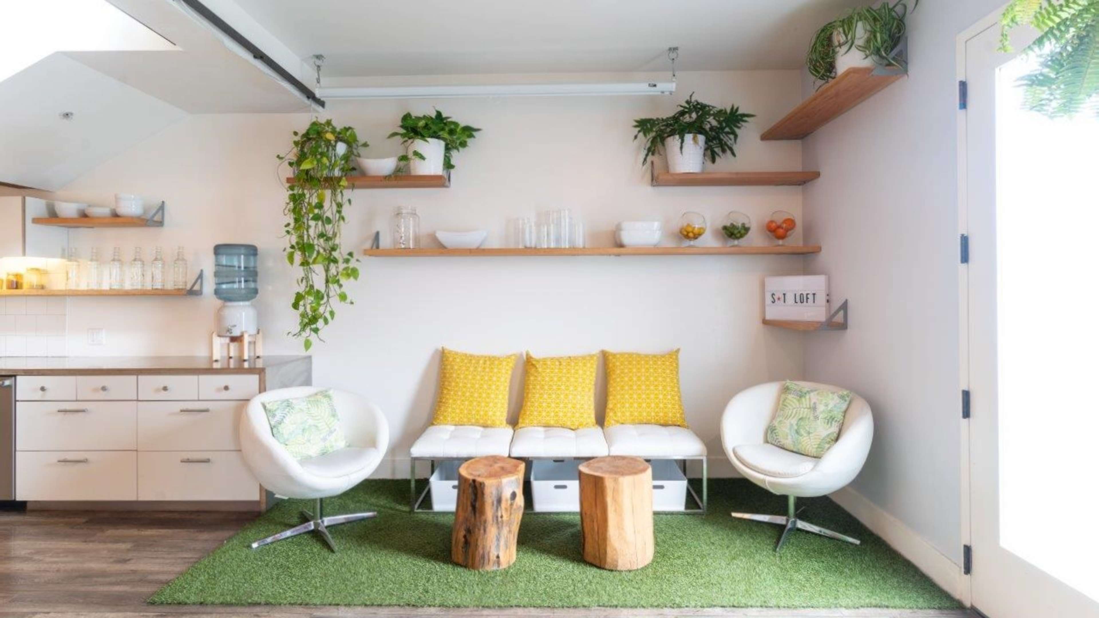 A modern indoor seating area with a white couch, two wooden stools, and shelves adorned with plants and decorative glassware.