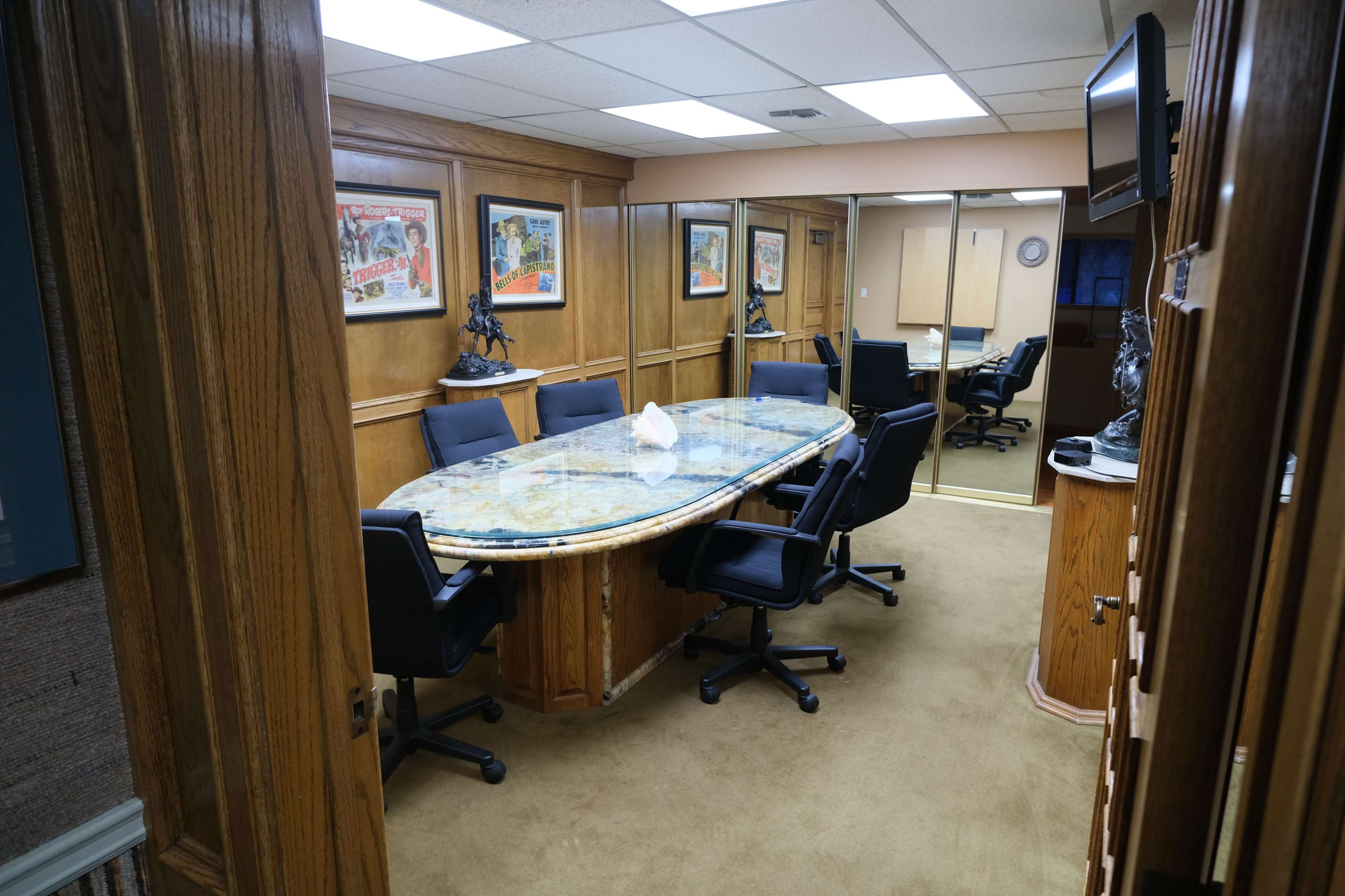 A wooden conference room with a large oval table surrounded by black chairs, decorated with framed posters on the walls.