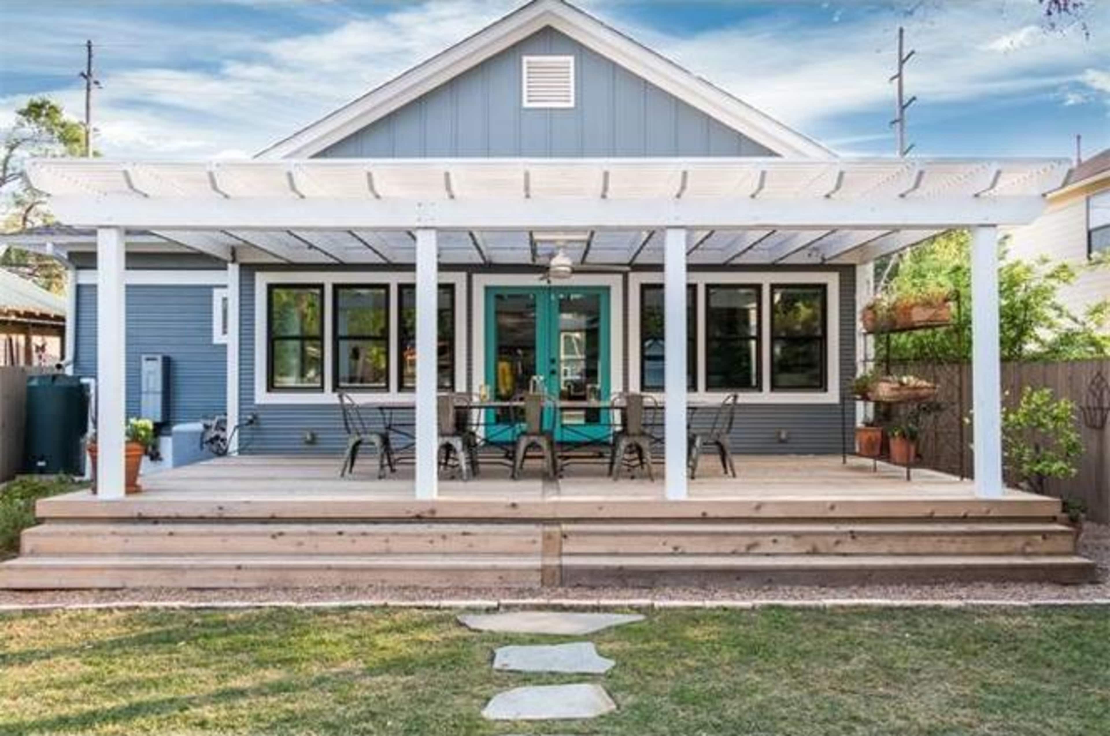 A blue house with a large wooden deck featuring a covered patio and a set of chairs and tables.