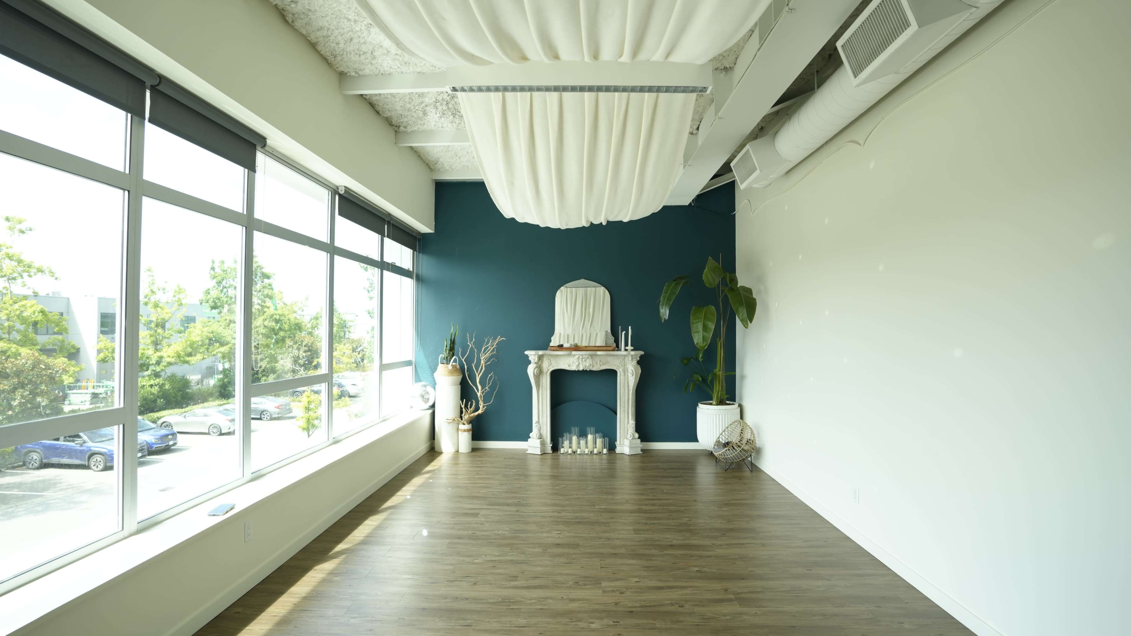 The image shows a spacious, airy room with large windows, a dark blue accent wall, and a decorative white mantelpiece with candles and a plant.
