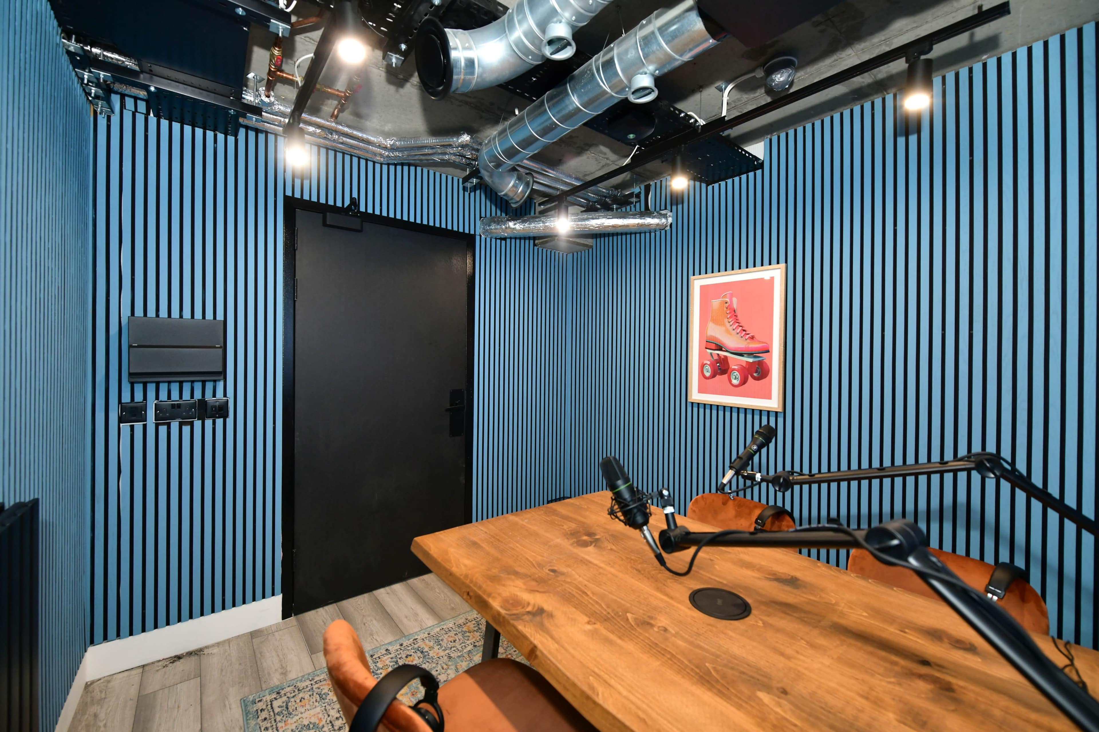 A recording studio with dark blue striped walls, a wooden table with microphones, and a door leading to the outside.