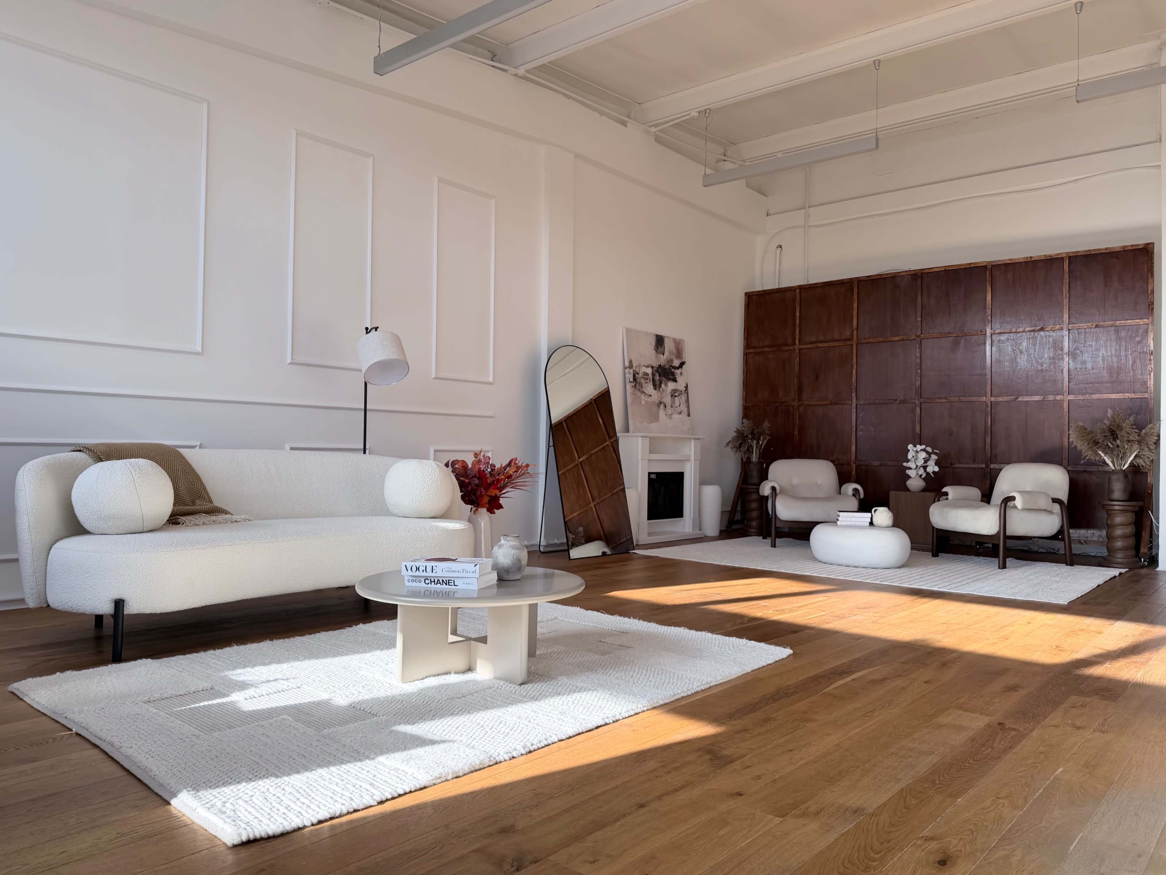 The image shows a bright, modern living space with a light-colored sofa, a coffee table, and two armchairs arranged around a decorative area rug.
