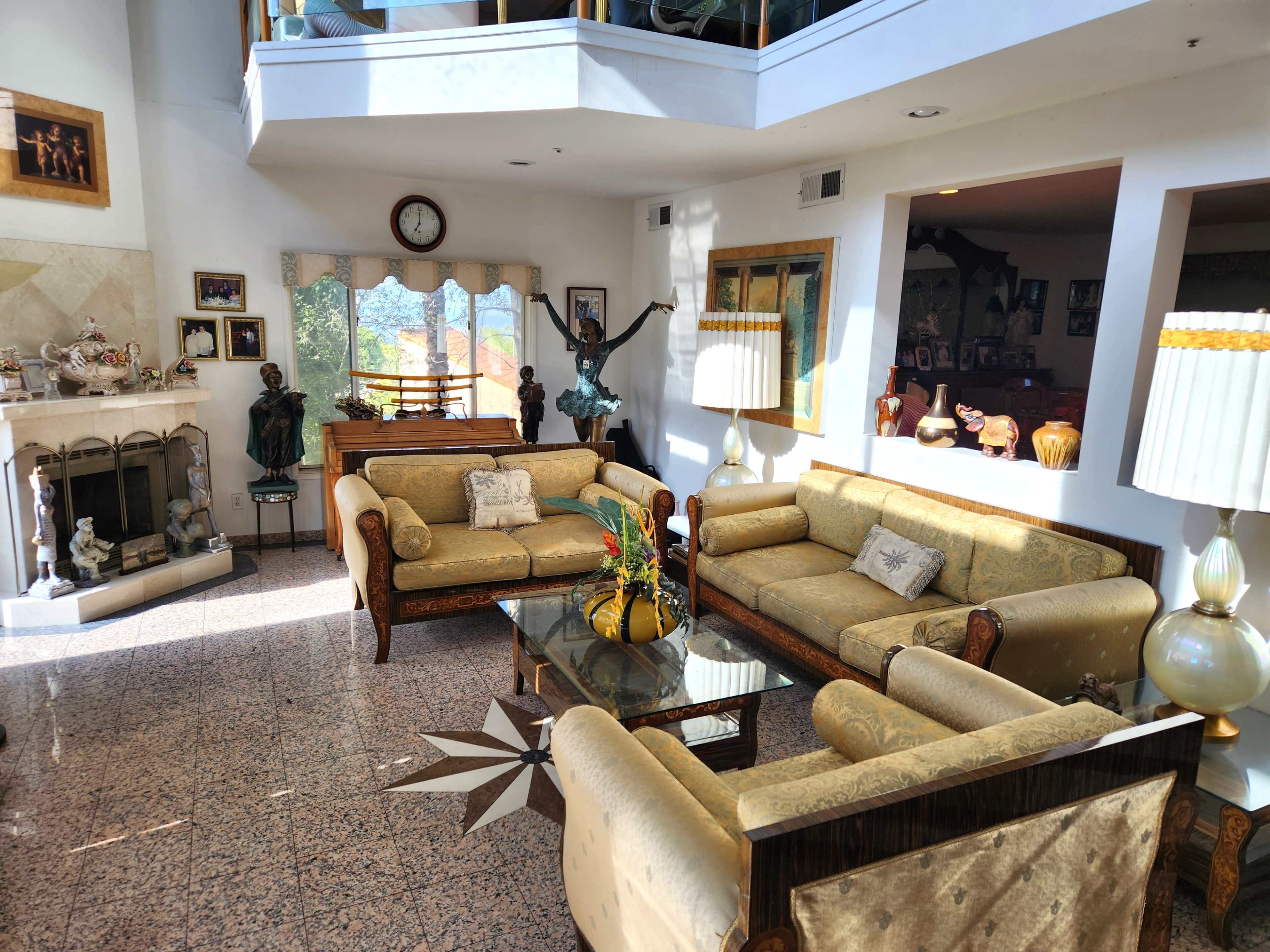 The living room features ornate furniture, a fireplace, and large windows that allow natural light to illuminate the space.