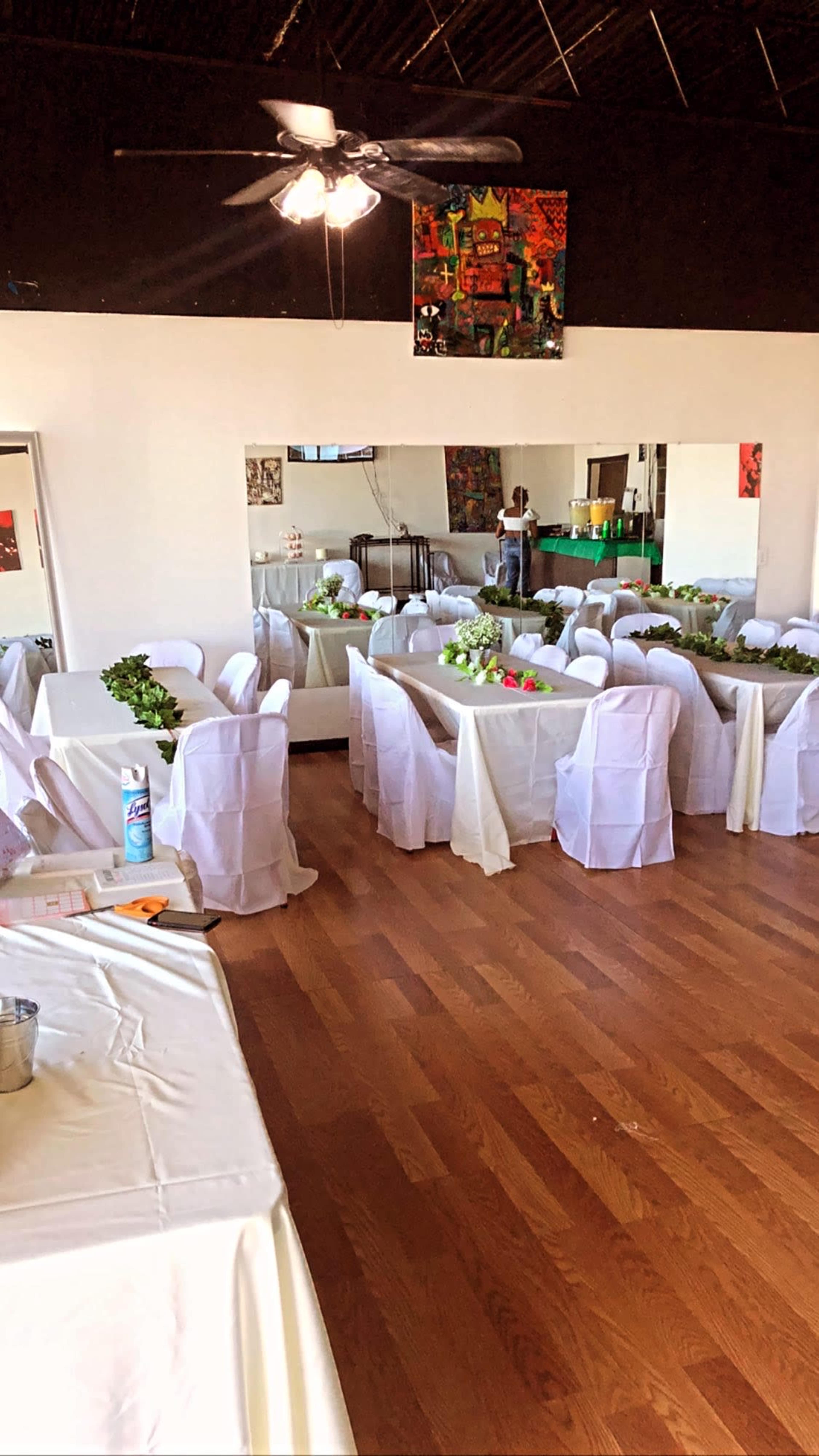 A decorated event space with tables covered in white tablecloths and chairs draped in white fabric, arranged for a gathering.