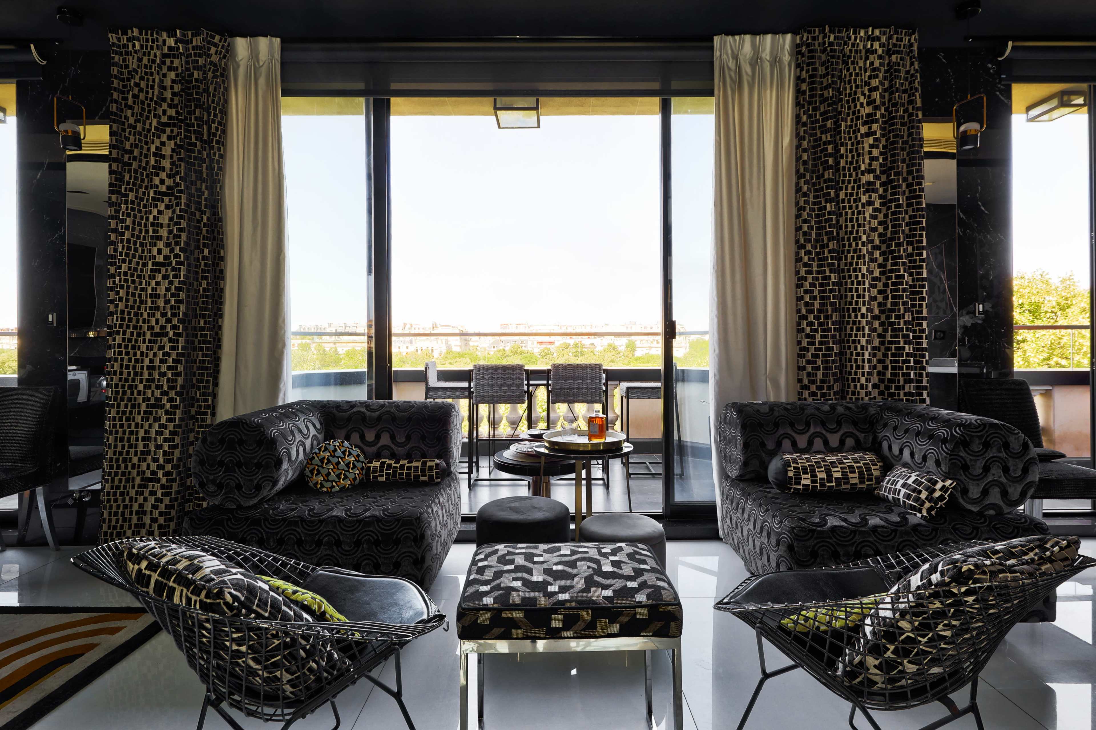 A modern lounge area features black patterned furniture and large windows overlooking an outdoor balcony.