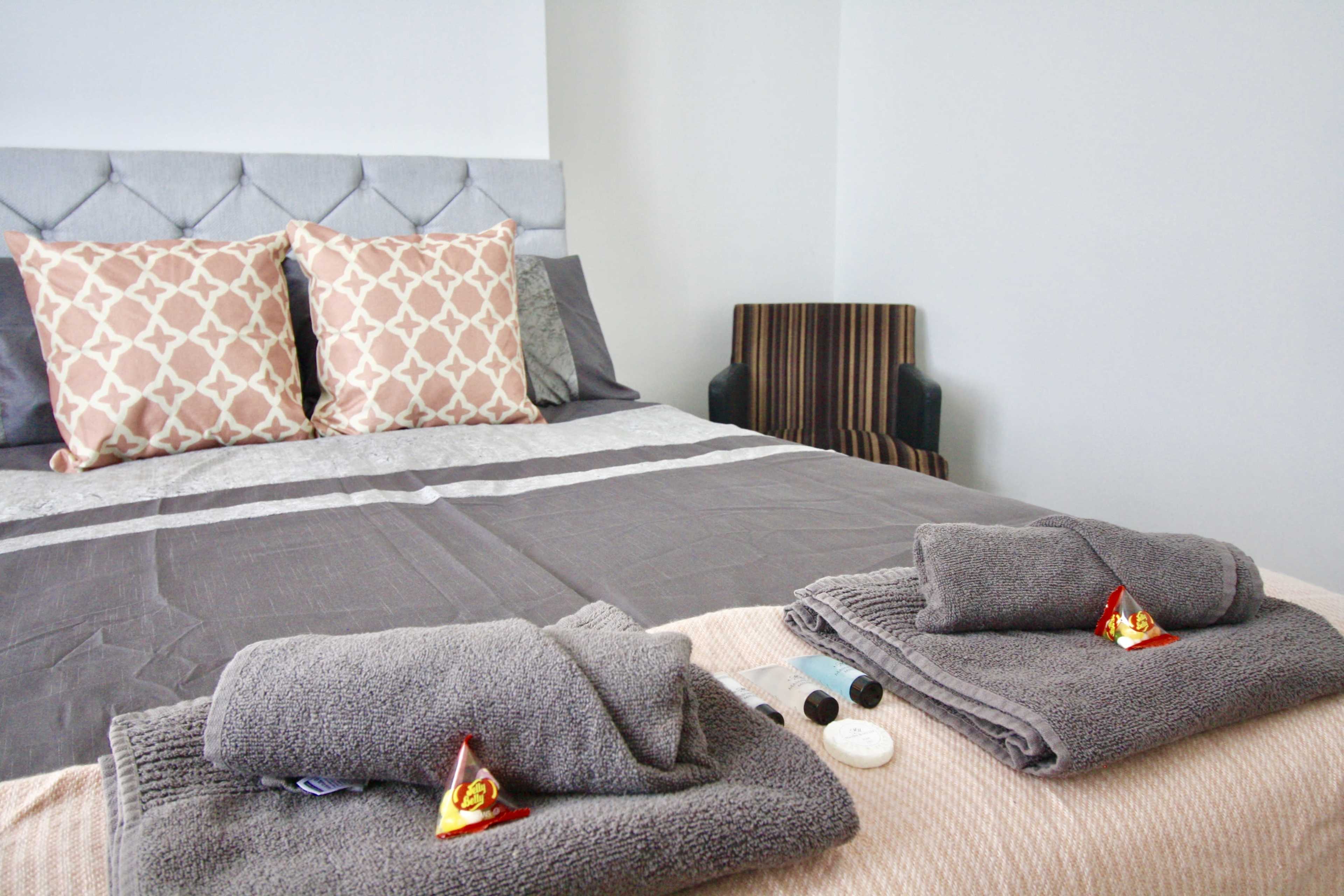A neatly arranged bed with decorative pillows, towels, and small amenities on the linens in a well-lit room.