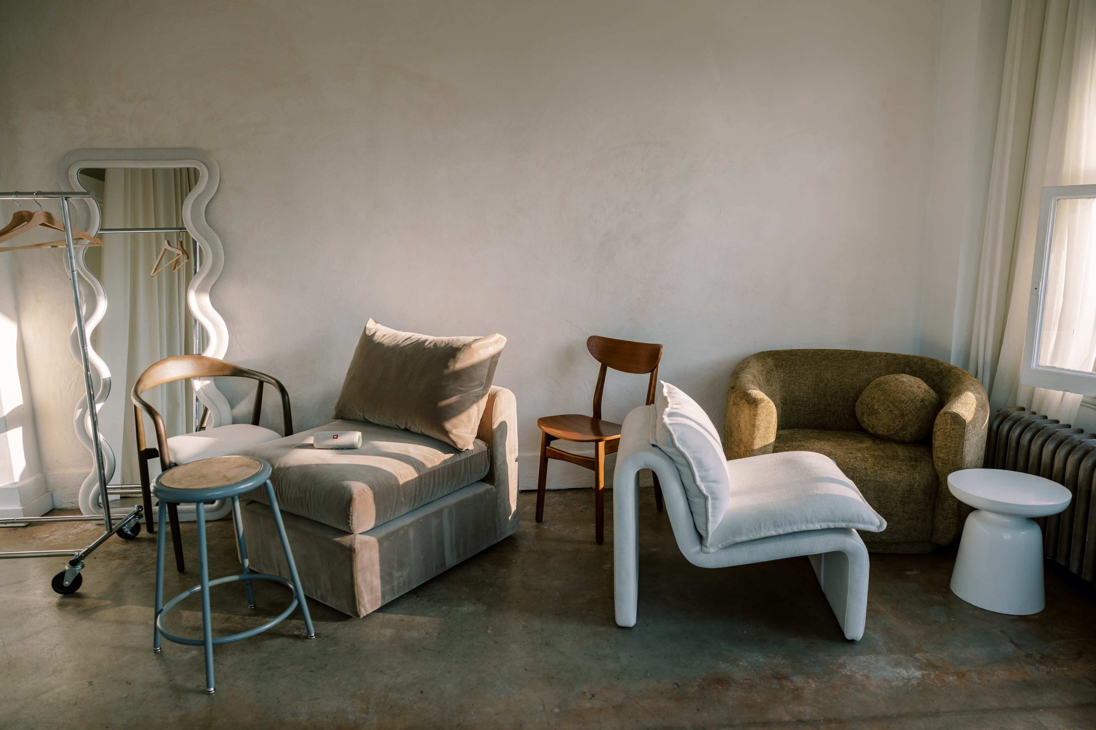 The image shows a room with a variety of furniture, including two sofas, a wooden chair, a metal stool, and a small white side table.