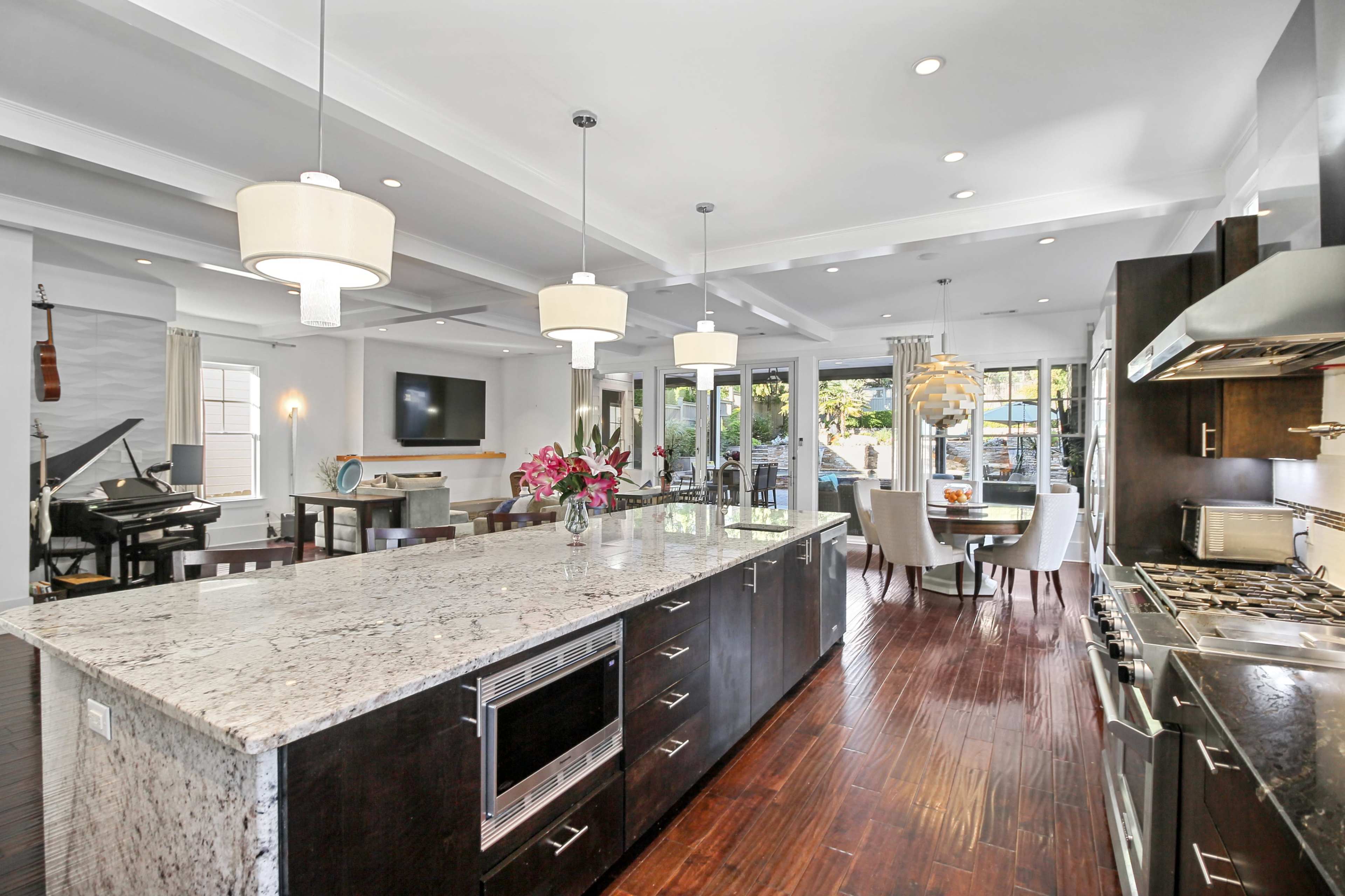 A modern kitchen and dining area featuring a large island with a dark wood finish, granite countertops, pendant lighting, and an open layout.