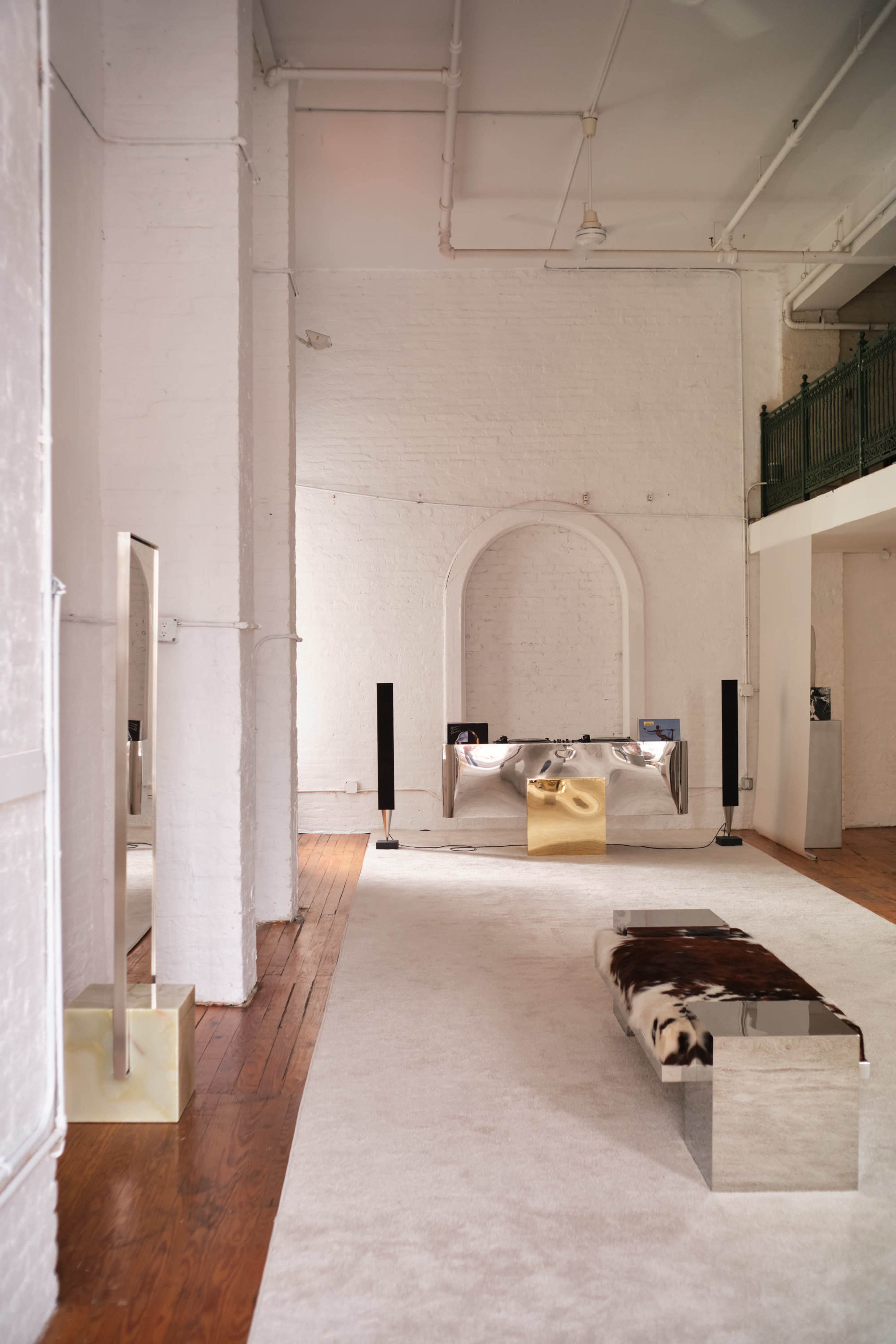 The image shows a spacious, minimalist interior with white walls, wooden floors, and modern furniture, including a bed and a reflective coffee table.