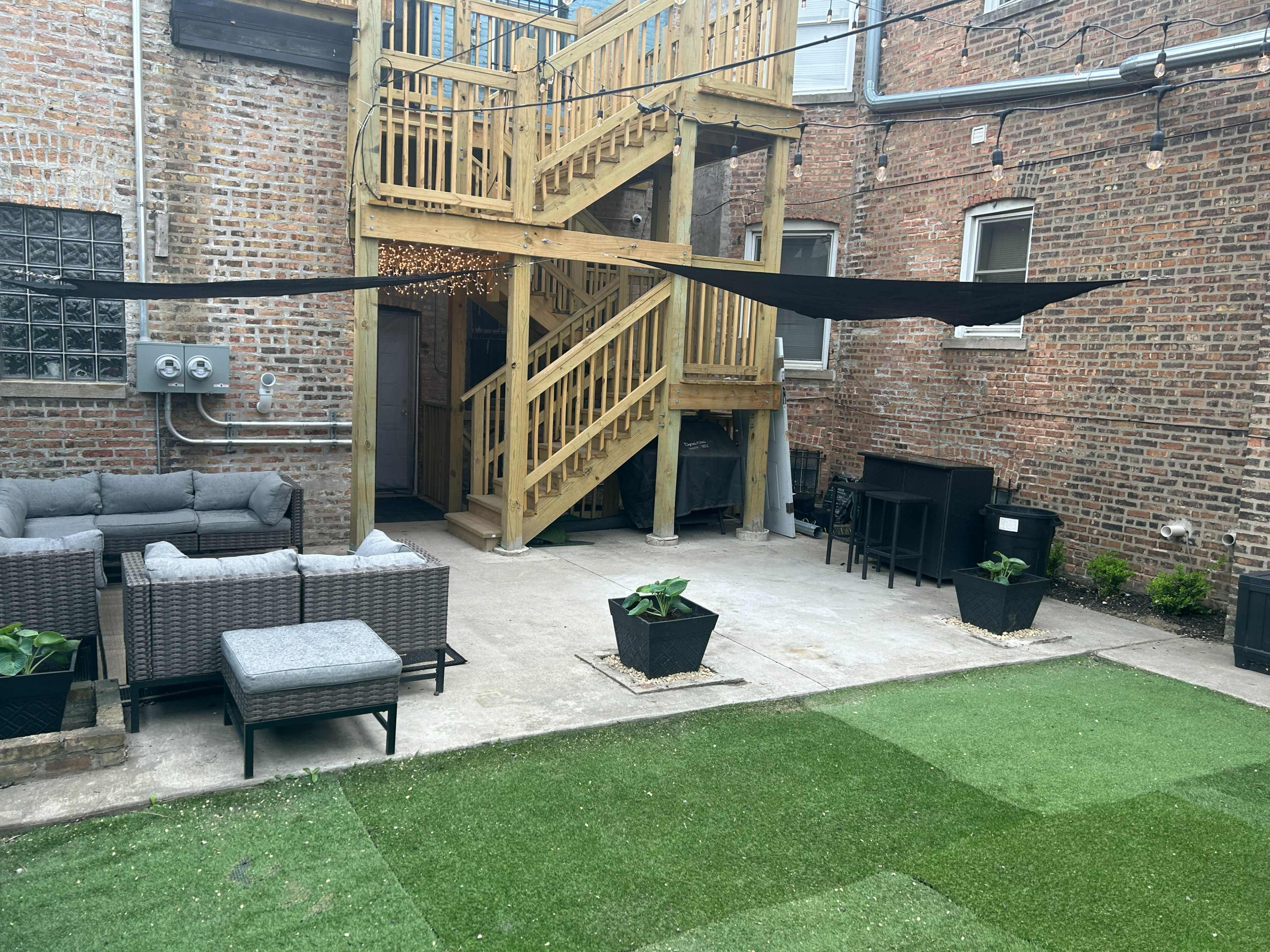 A fenced backyard area featuring a wooden staircase, outdoor furniture, and a lawn with artificial grass.