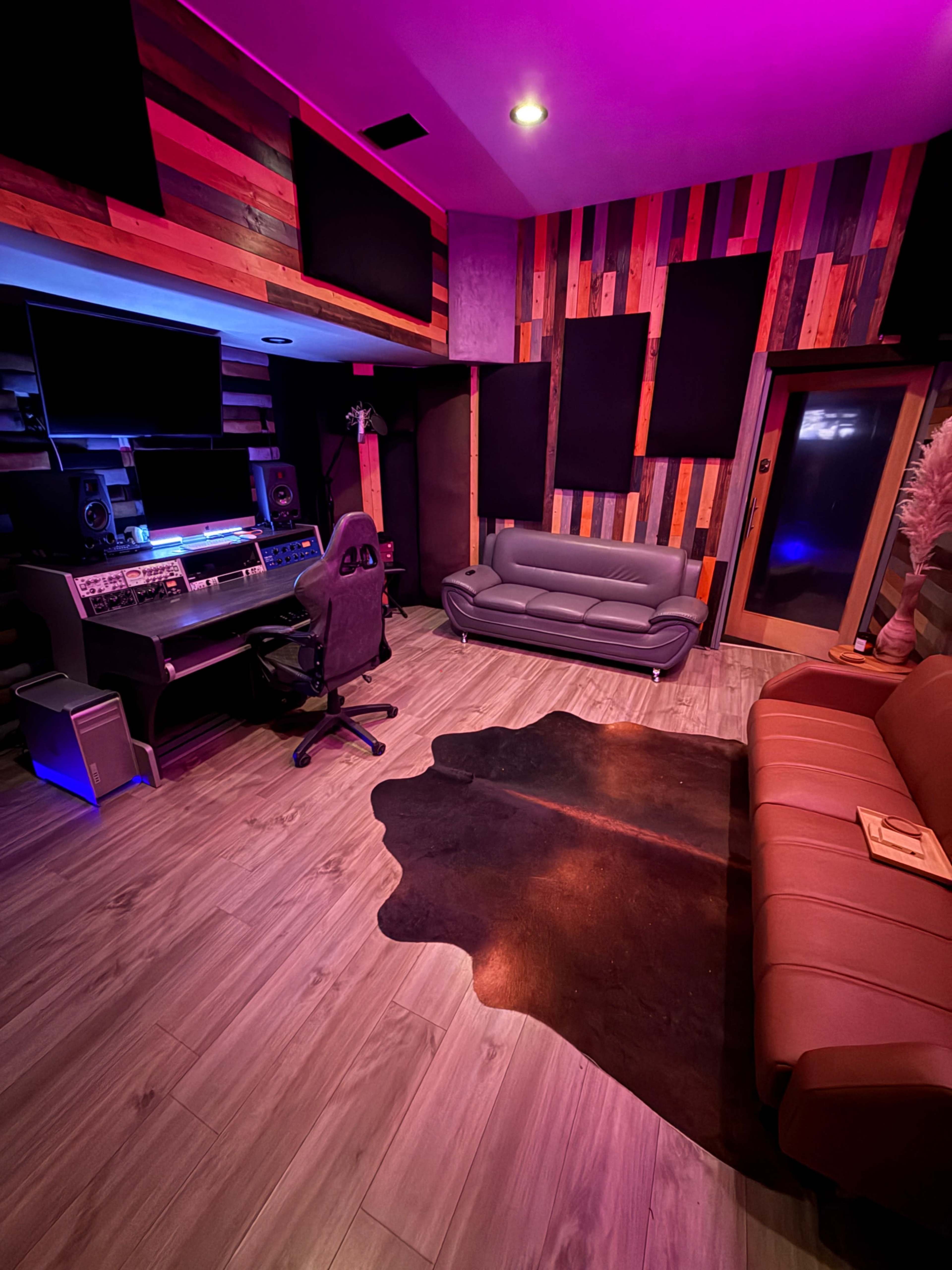 The image shows a music studio with a mixing desk, two seating areas, soundproof panels on the walls, and purple lighting.