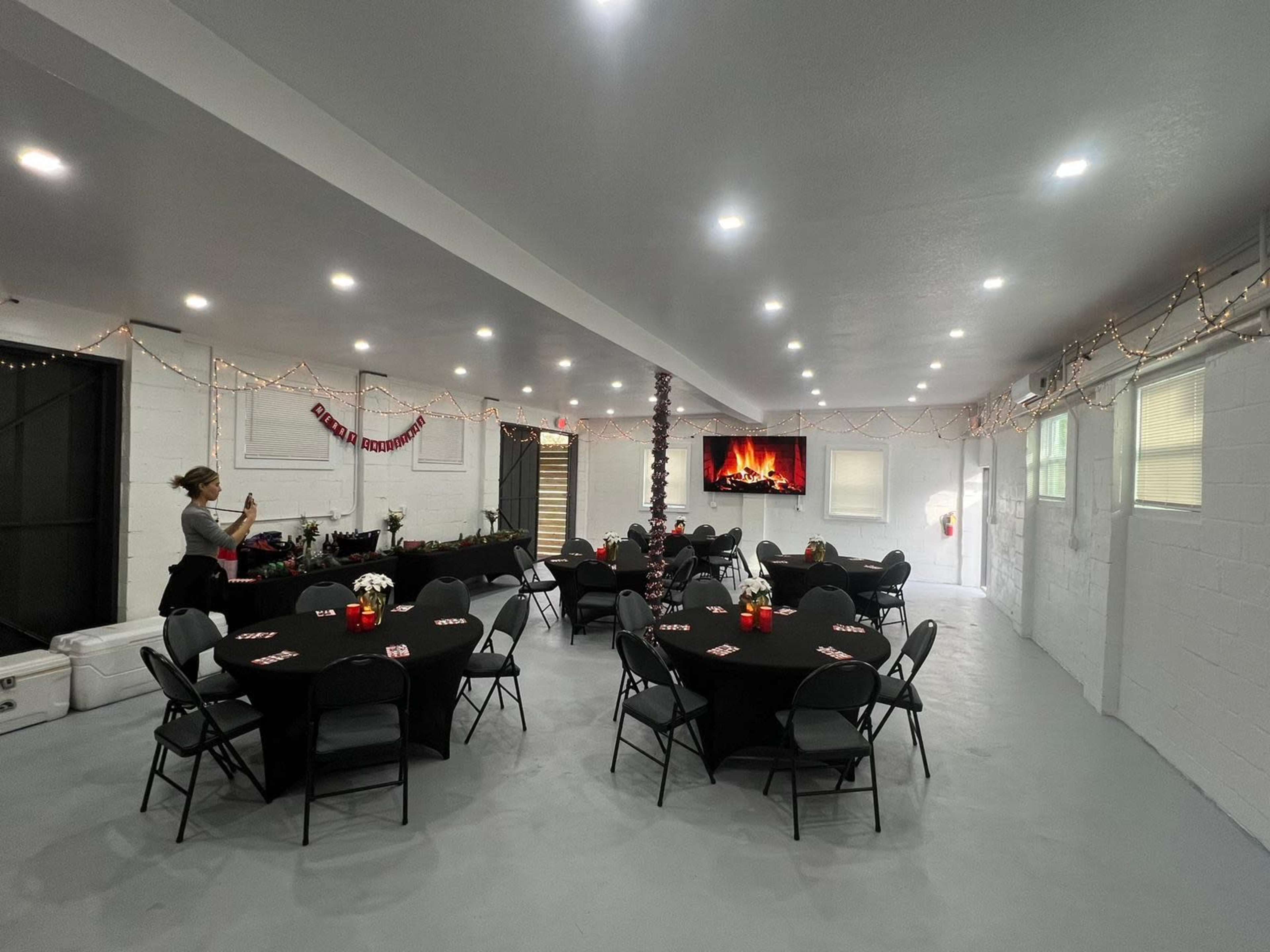 The room features several round tables with black tablecloths, decorated with red centerpieces, and is illuminated by bright overhead lights.