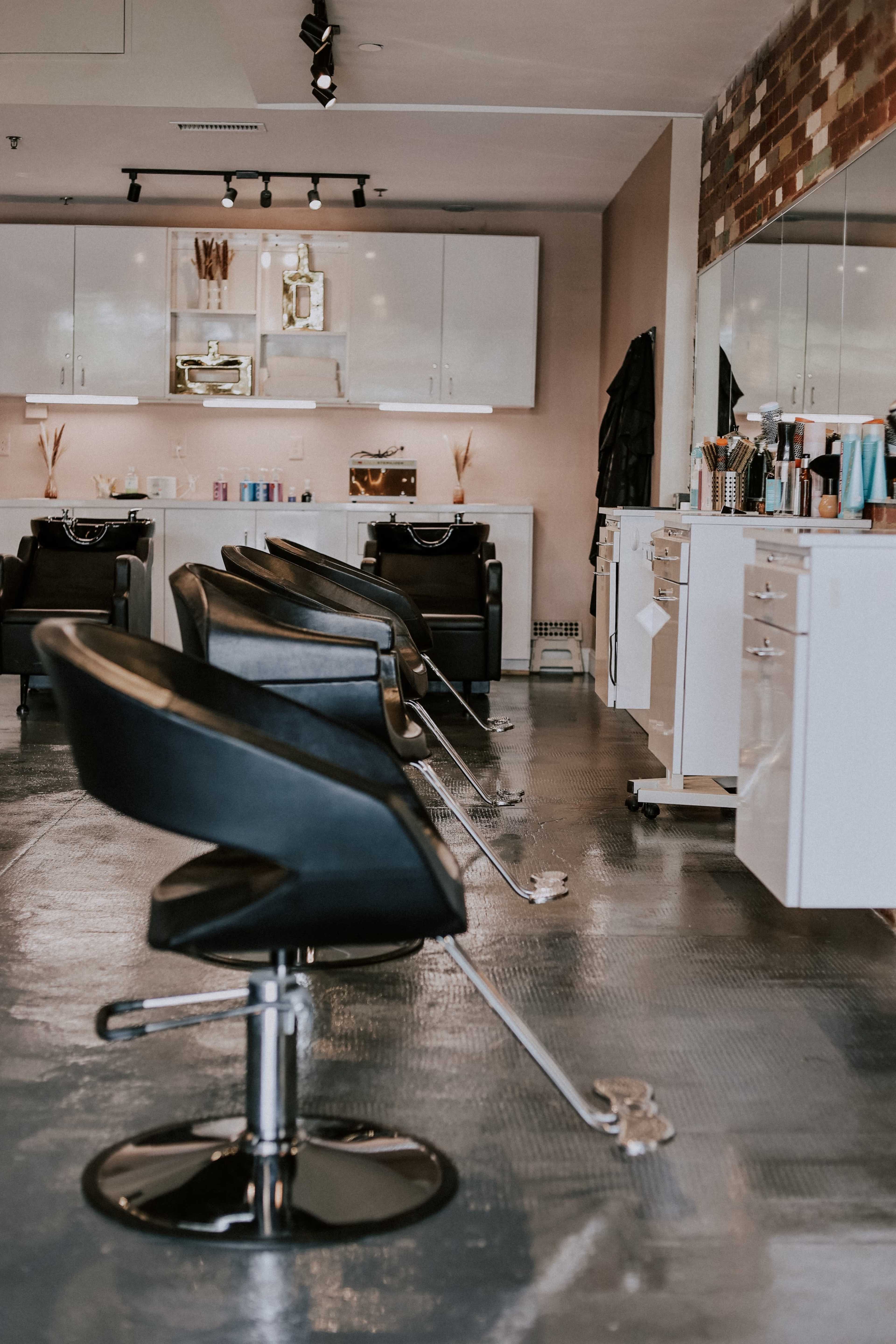 A modern hair salon with several black styling chairs arranged in front of mirrors and cabinets.