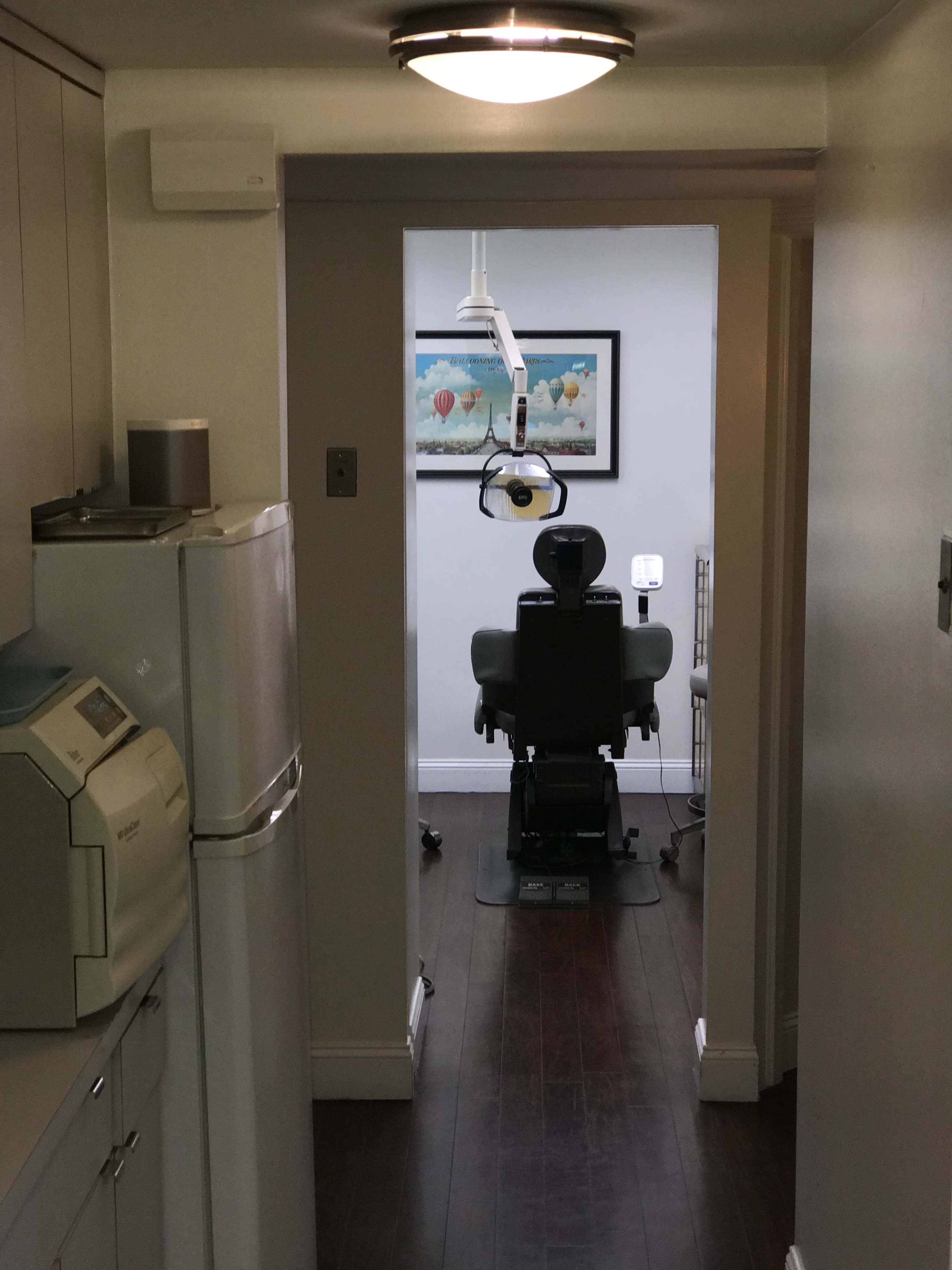 The image shows a hallway leading to a dental examination room, featuring dental equipment and a chair.
