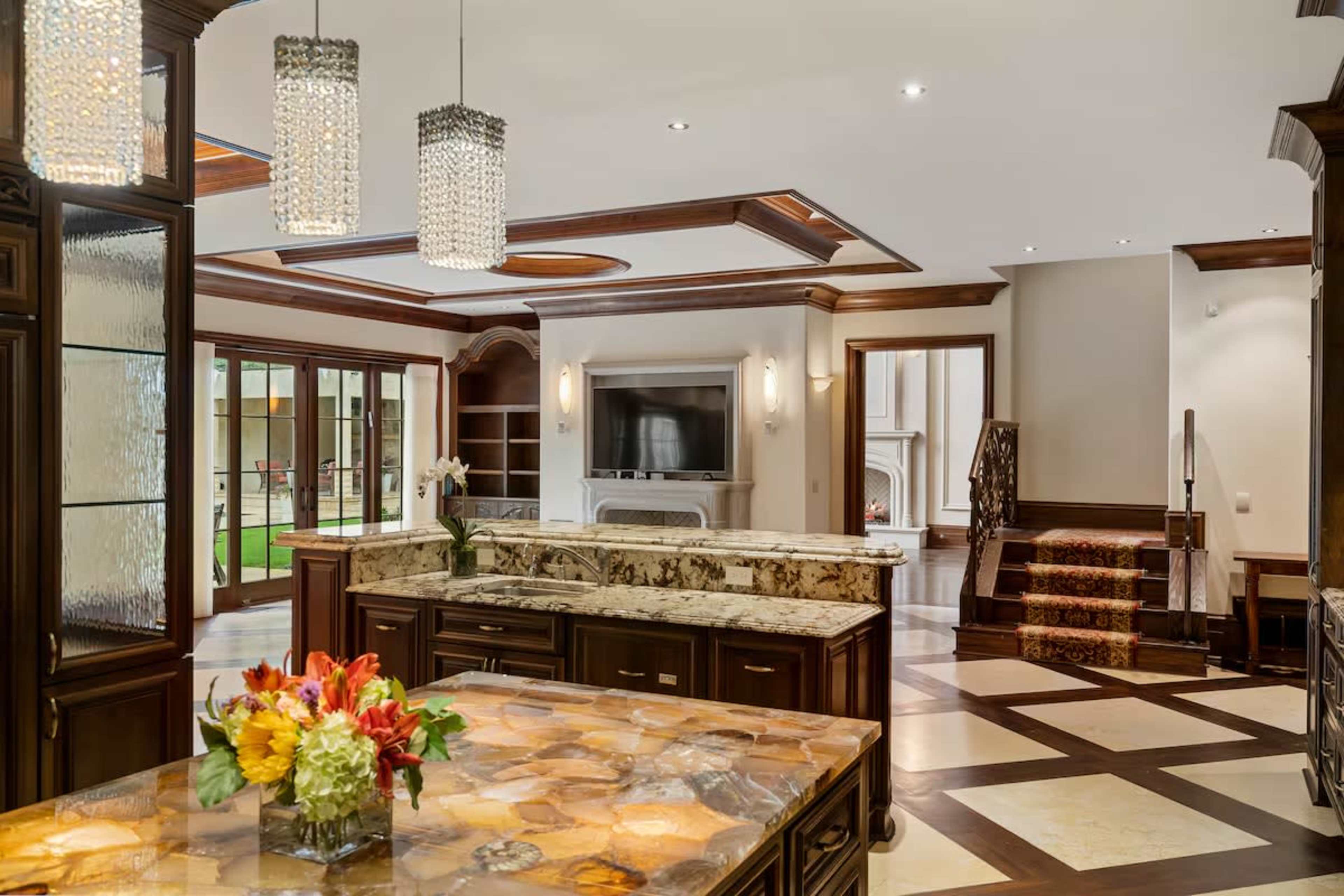 The image shows a spacious modern kitchen with dark wooden cabinets, a large granite countertop, and elegant pendant lighting.