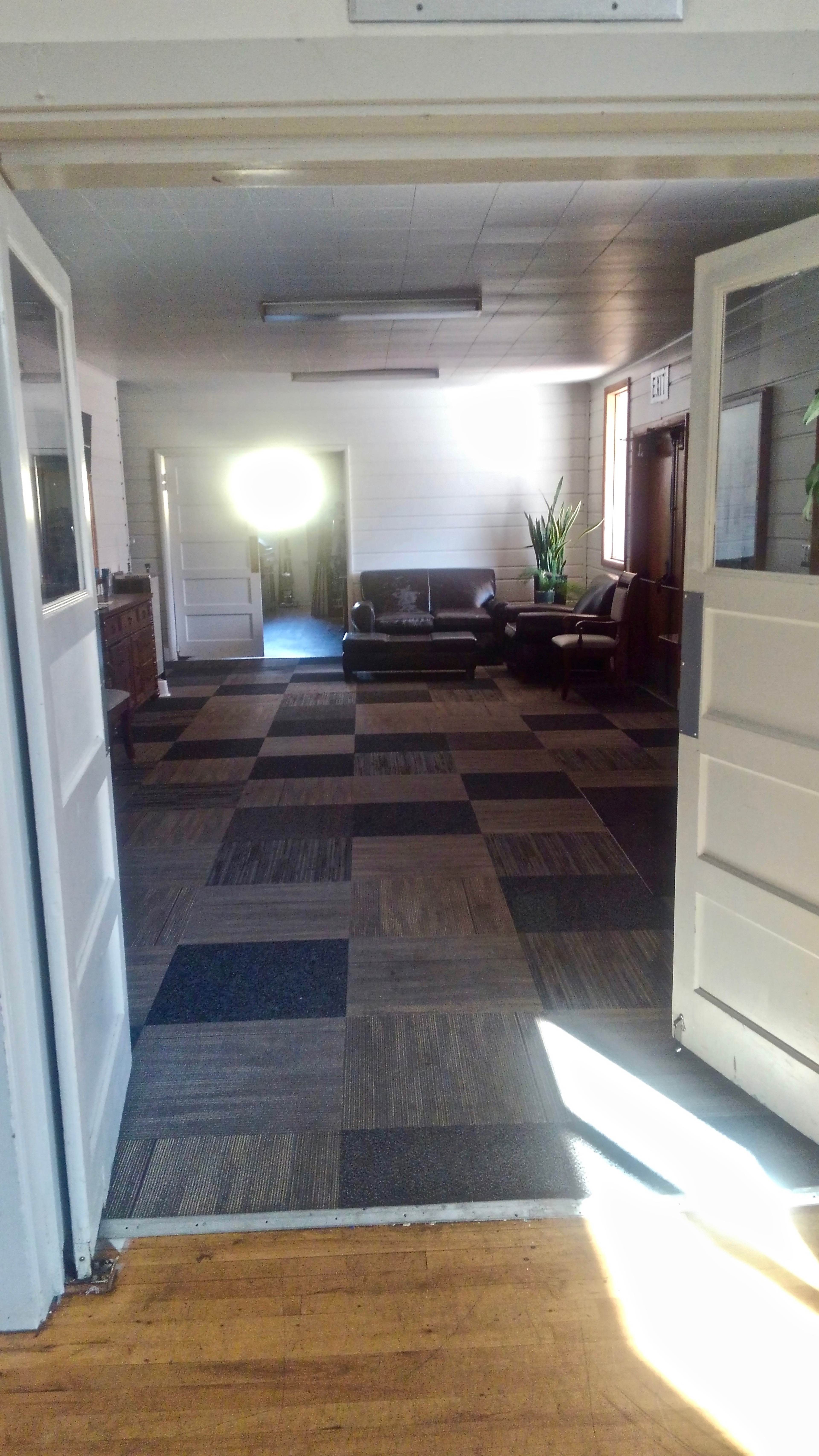 The image shows a spacious room with a patterned carpet, a sofa in the background, and natural light coming through a window.