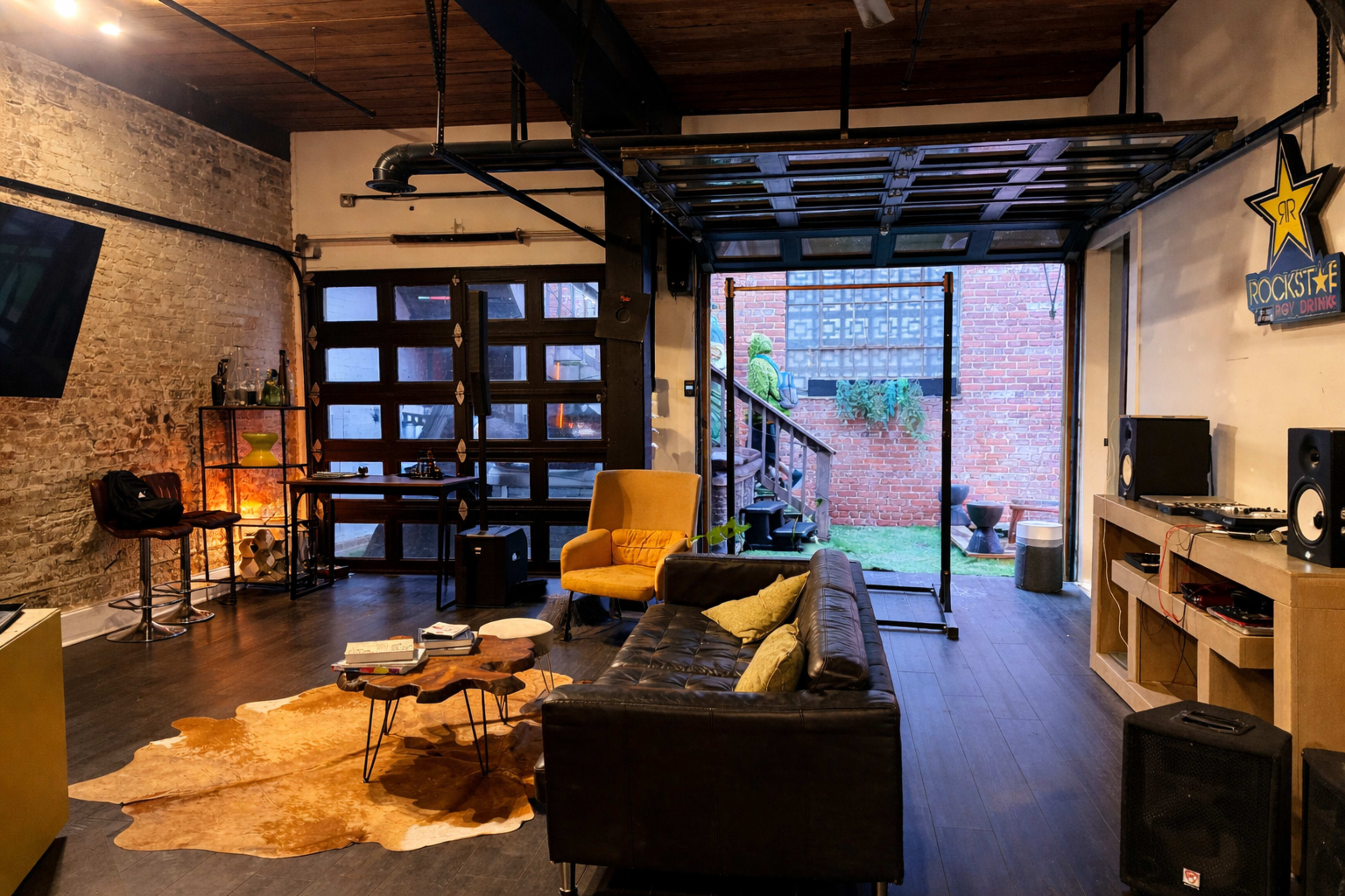 The image depicts a stylish living space with an open layout, featuring a brown leather sofa, a coffee table, and a large glass door leading to an outdoor area with a staircase.