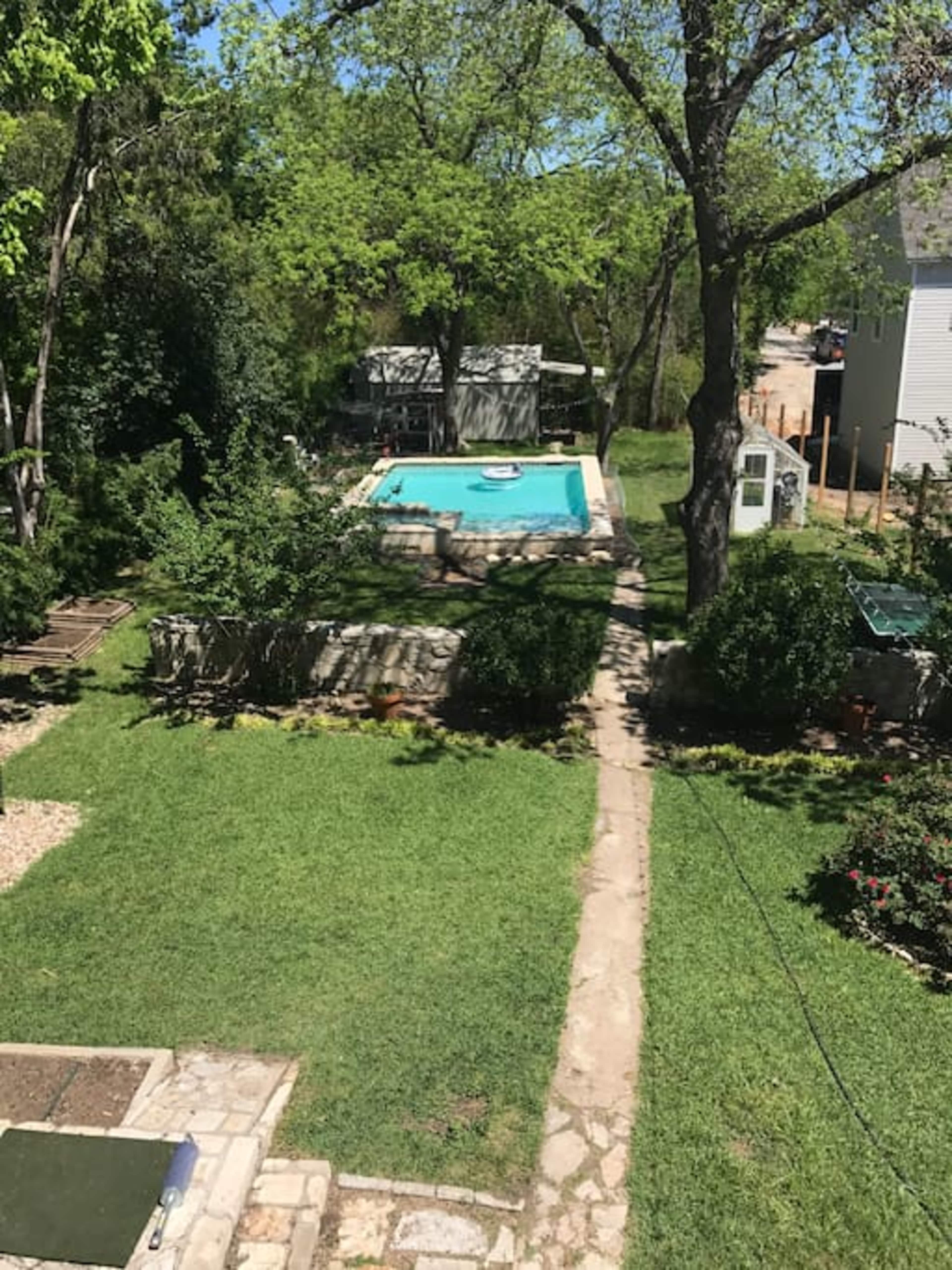 A backyard with a swimming pool surrounded by green grass and garden paths.