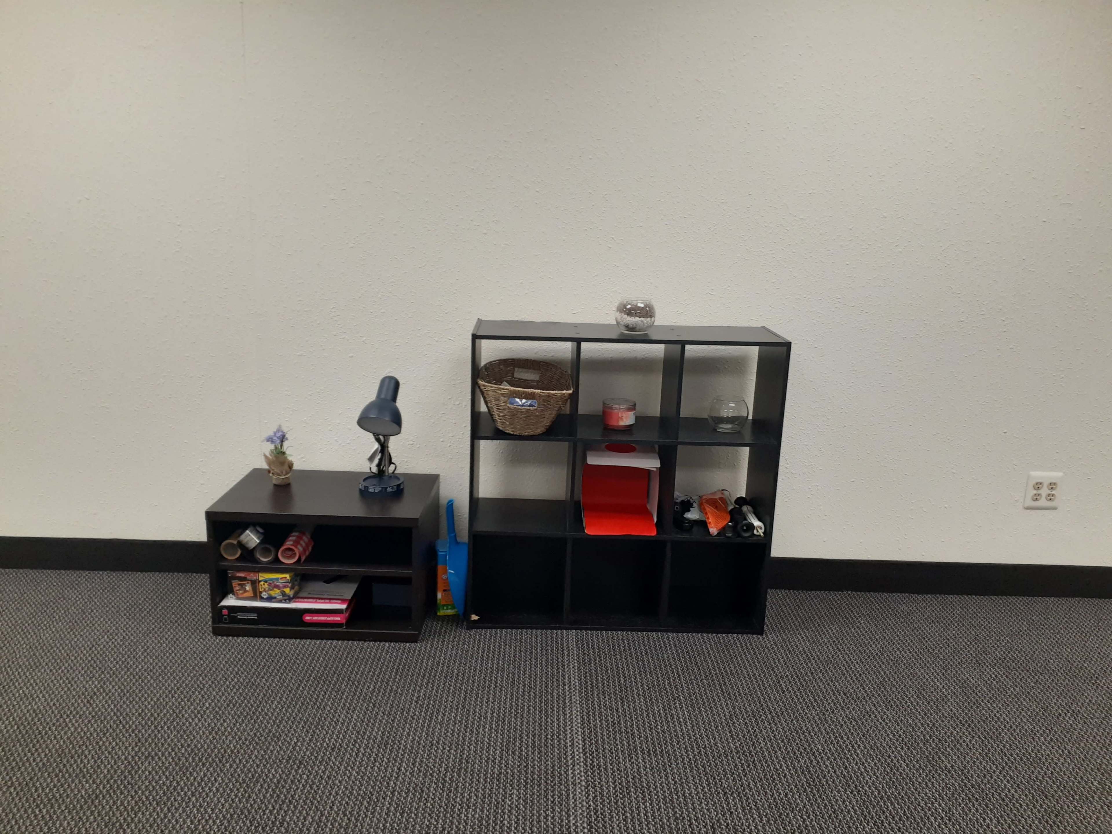 Two black shelves against a plain wall, one featuring a lamp and decorative items, and the other displaying various objects.