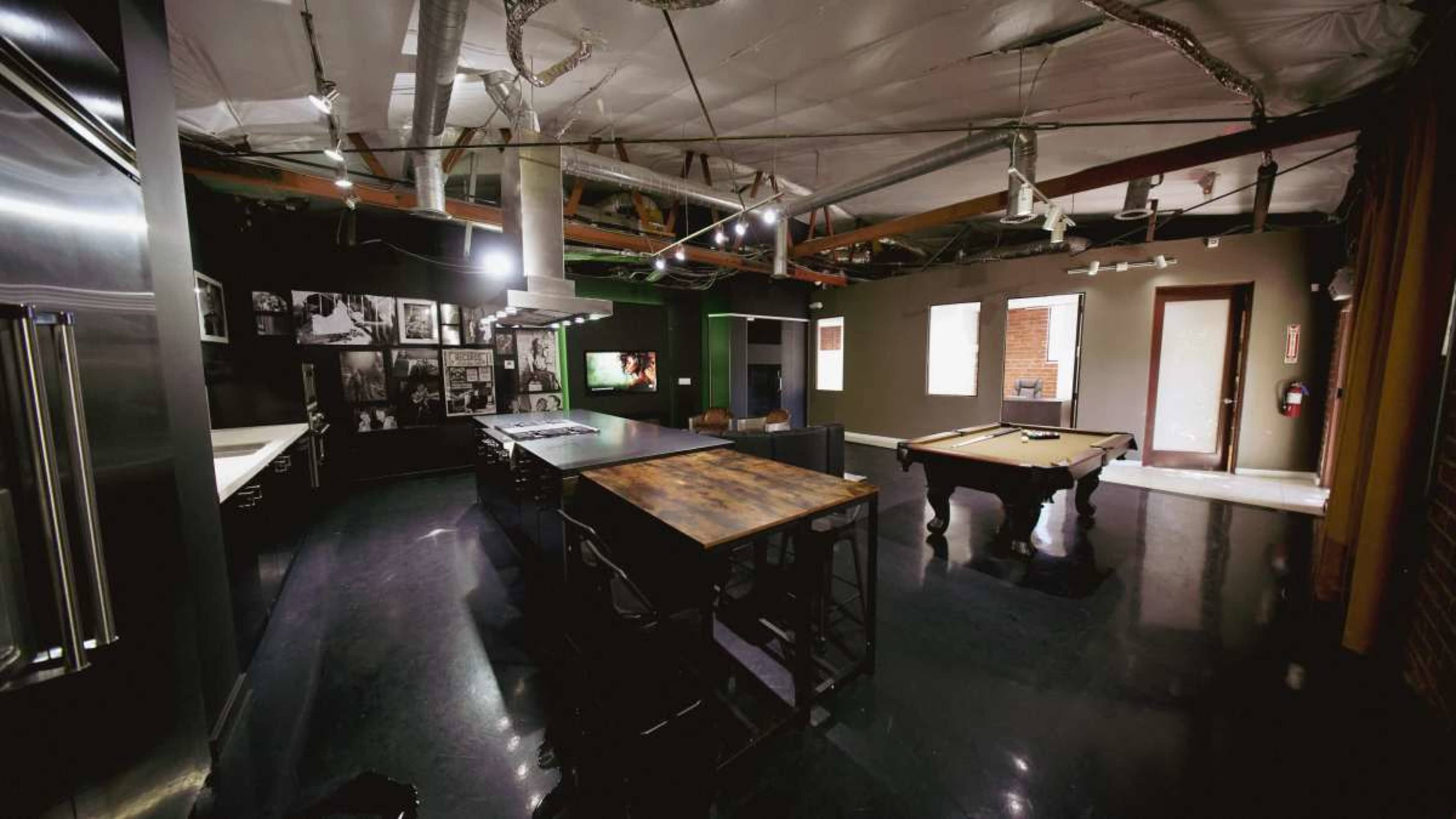 The image shows a spacious game room featuring a pool table, a dining table, and walls adorned with black-and-white photographs.