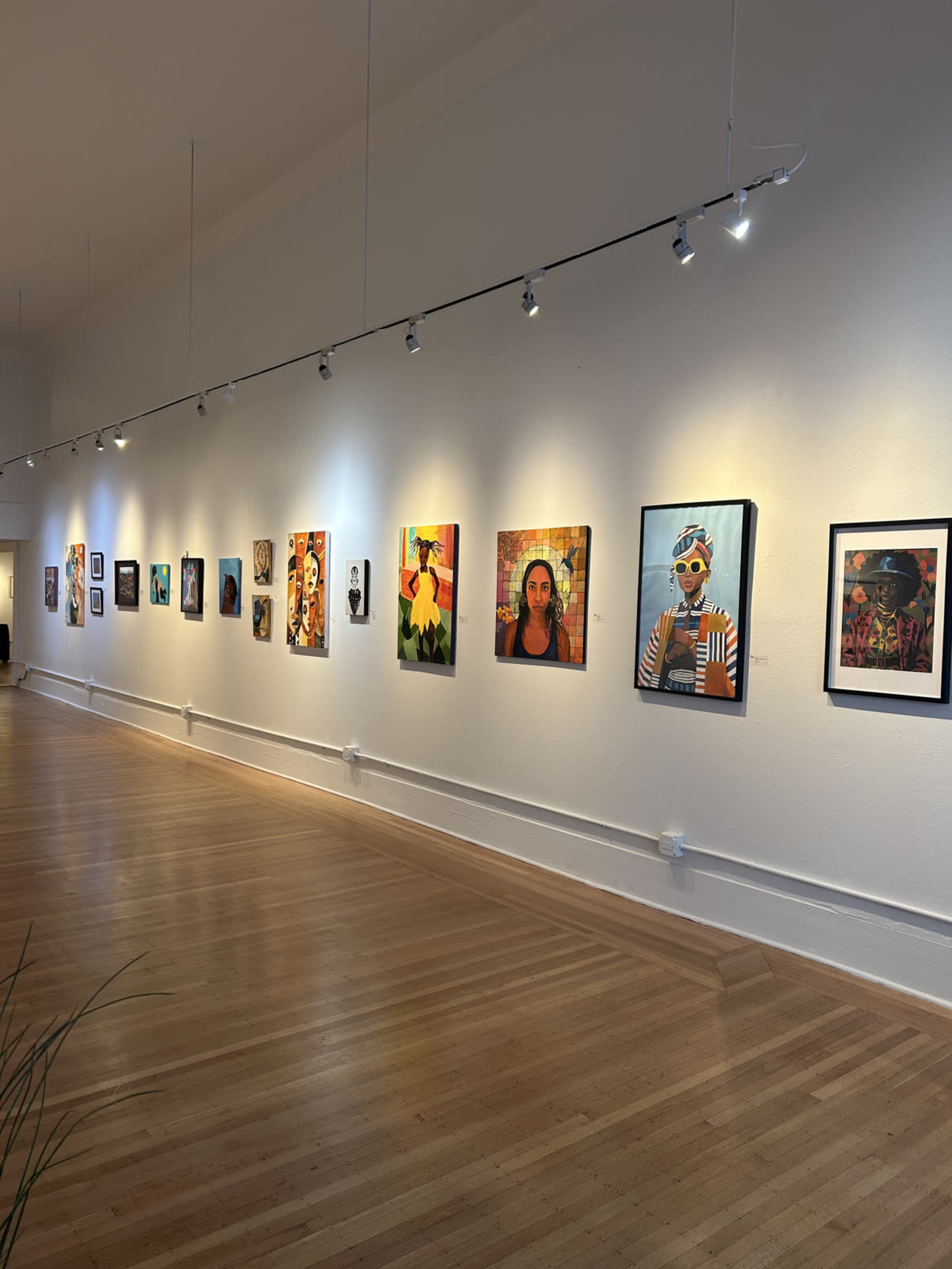 An art gallery features a row of colorful portraits displayed on a white wall, illuminated by track lighting.