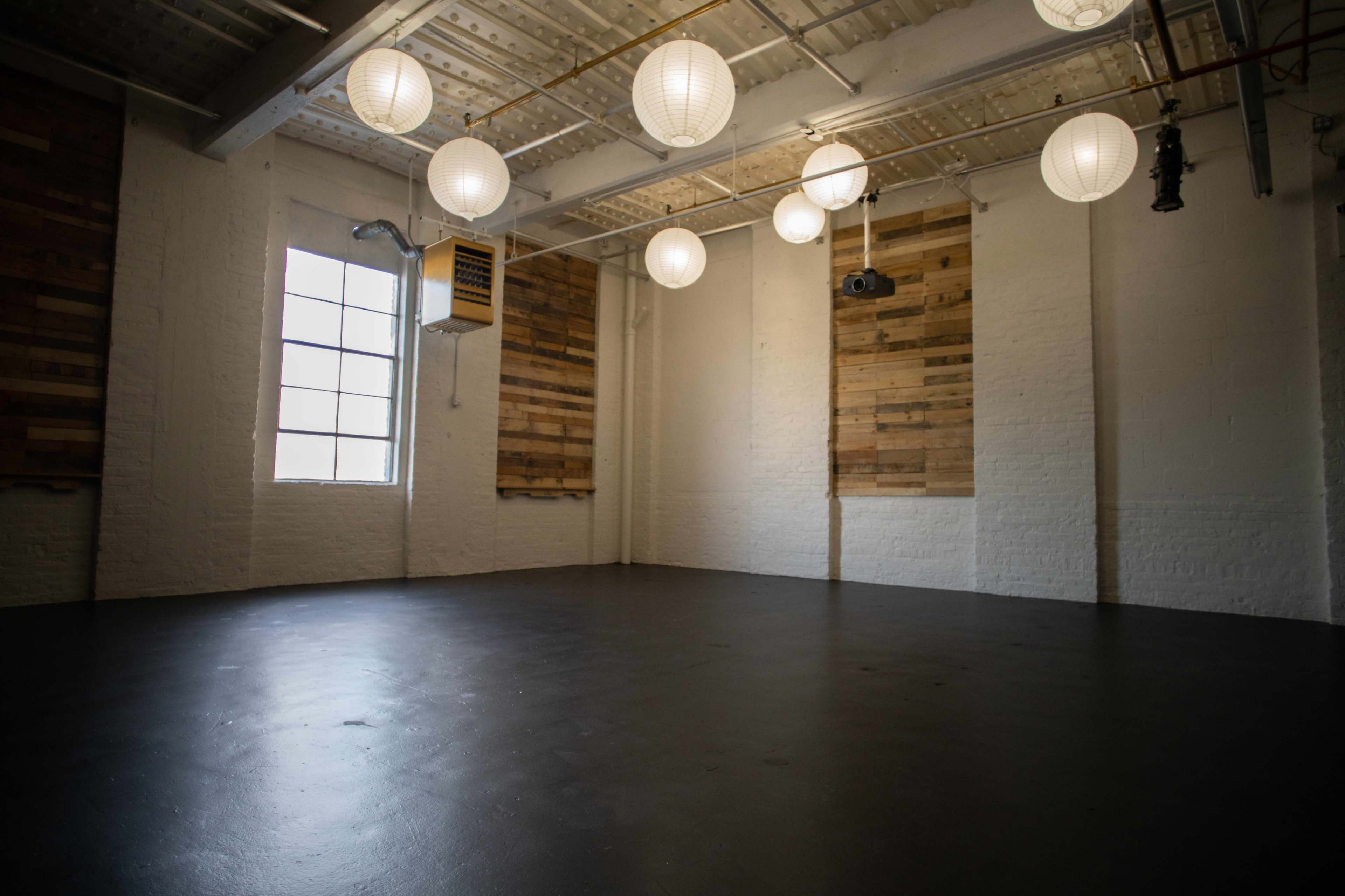 A bright, empty room with wooden wall accents and several hanging lantern lights.