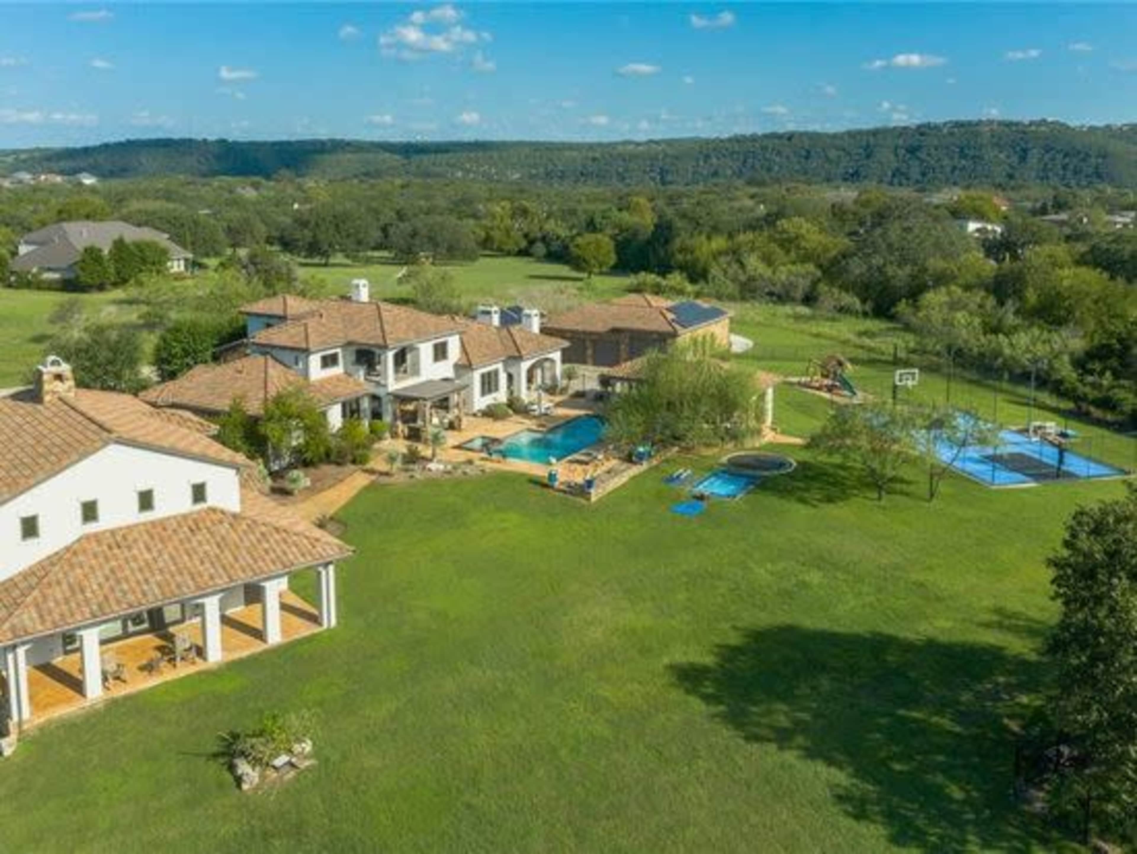 A spacious property features multiple buildings, a swimming pool, and a basketball court set against a backdrop of rolling hills.