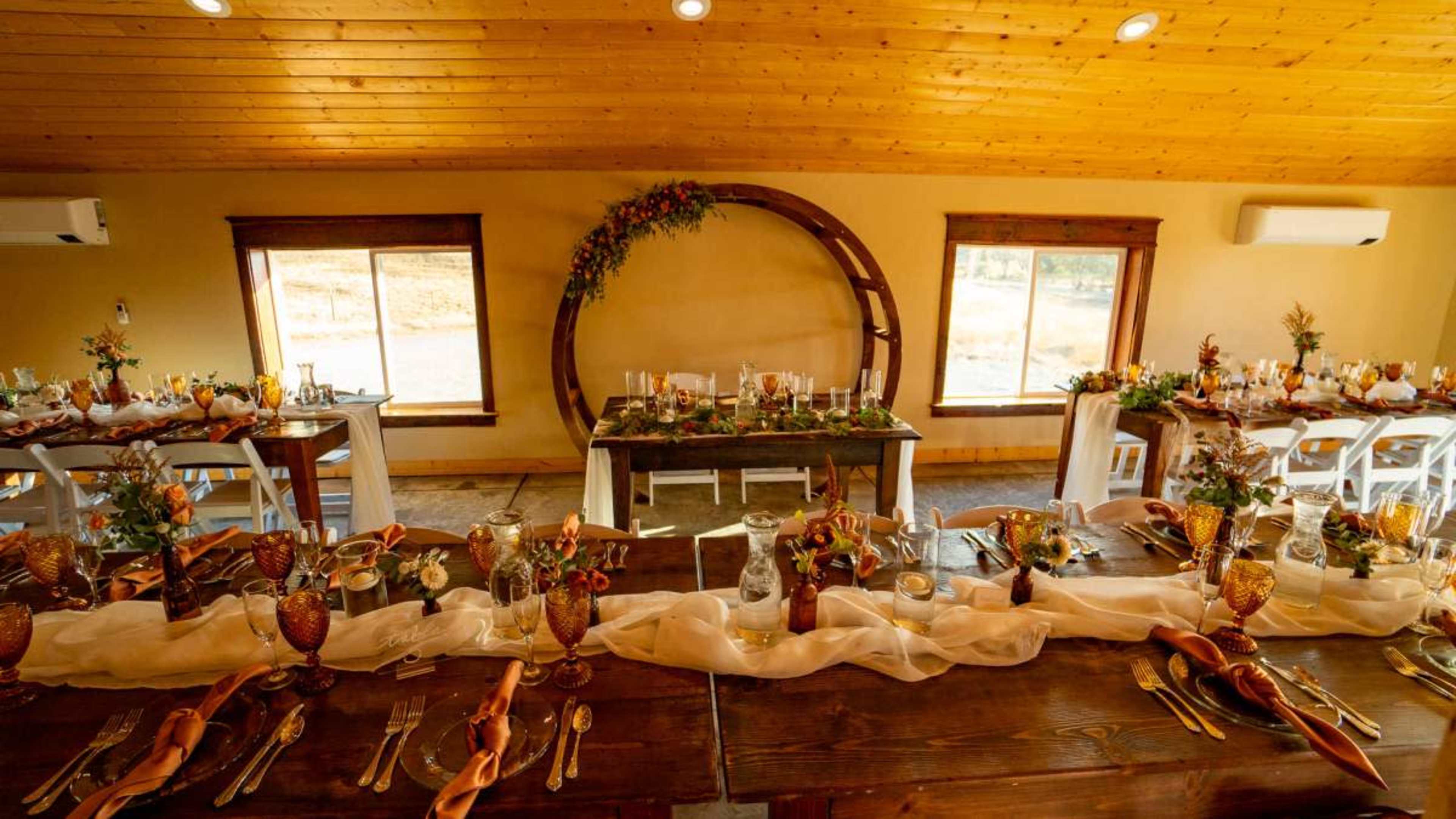 A banquet setting features elegantly arranged tables with floral centerpieces and a circular backdrop in a warmly lit room.