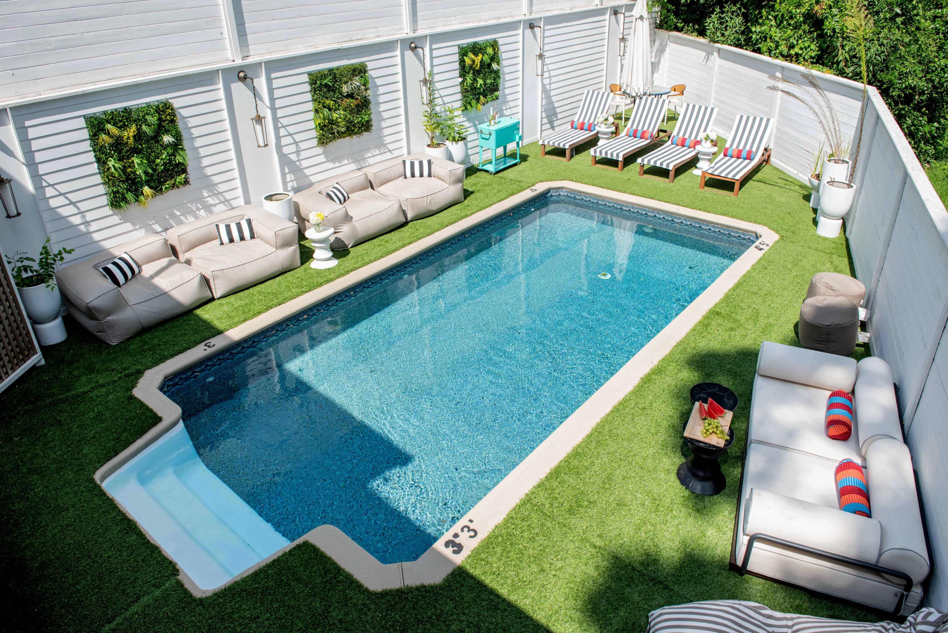 A rectangular swimming pool surrounded by green artificial grass and outdoor seating areas, including lounge chairs and sofas.