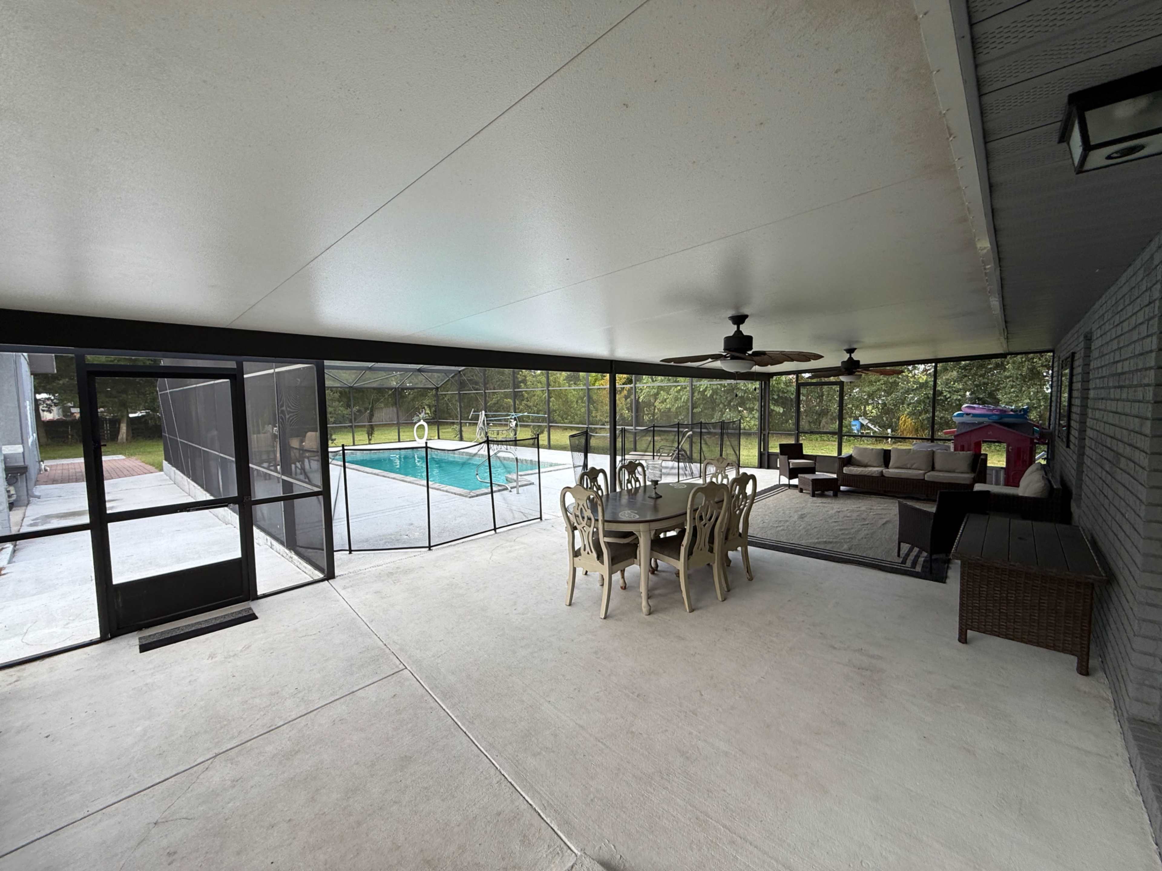 The image shows a screened patio with a dining table and chairs facing a swimming pool.