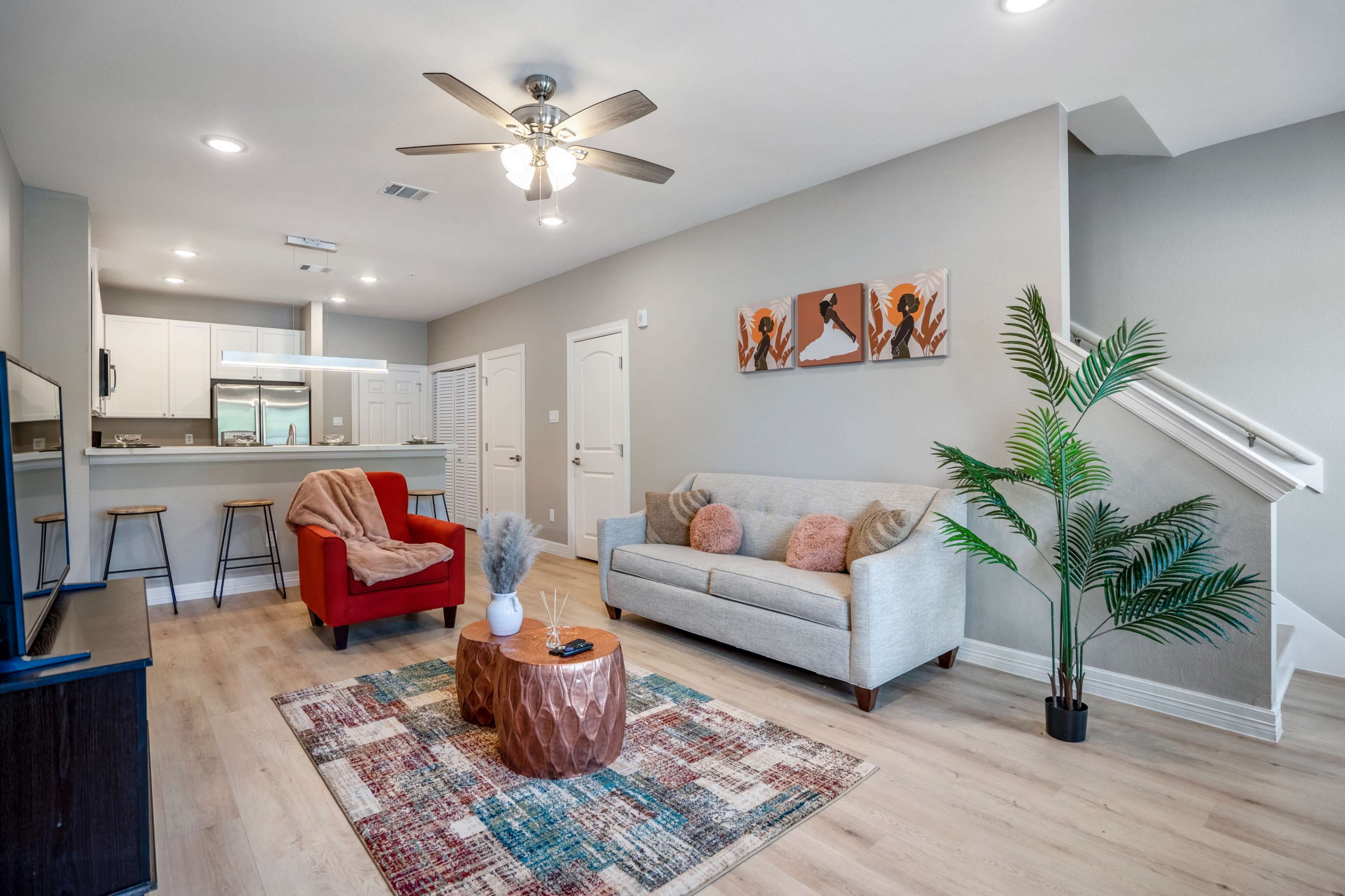 A modern living room with a gray sofa, a red armchair, a coffee table, and a ceiling fan, leading to an open kitchen area.