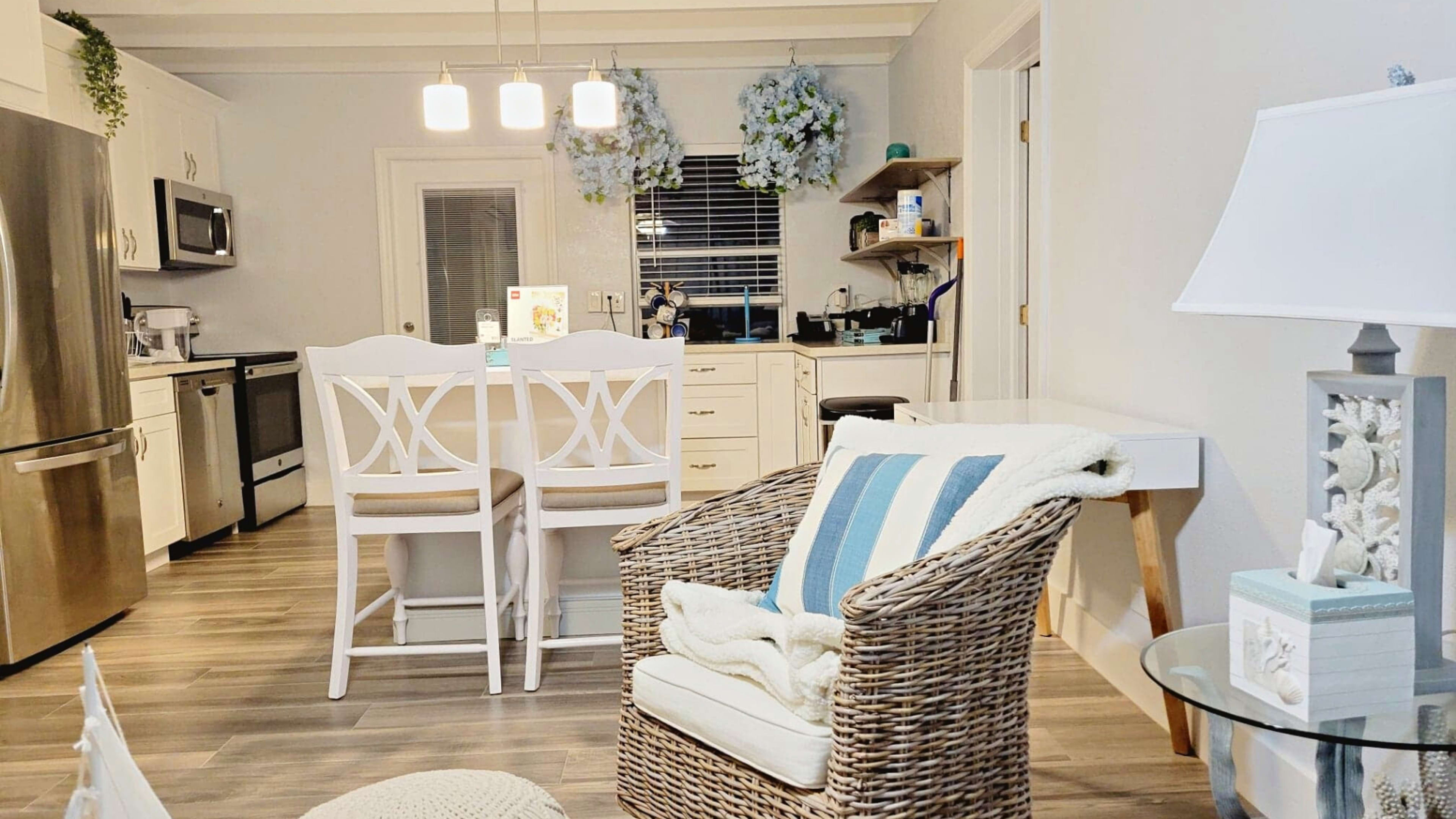 A modern living space with a wicker chair, dining area with high-backed chairs, and a kitchen in the background.