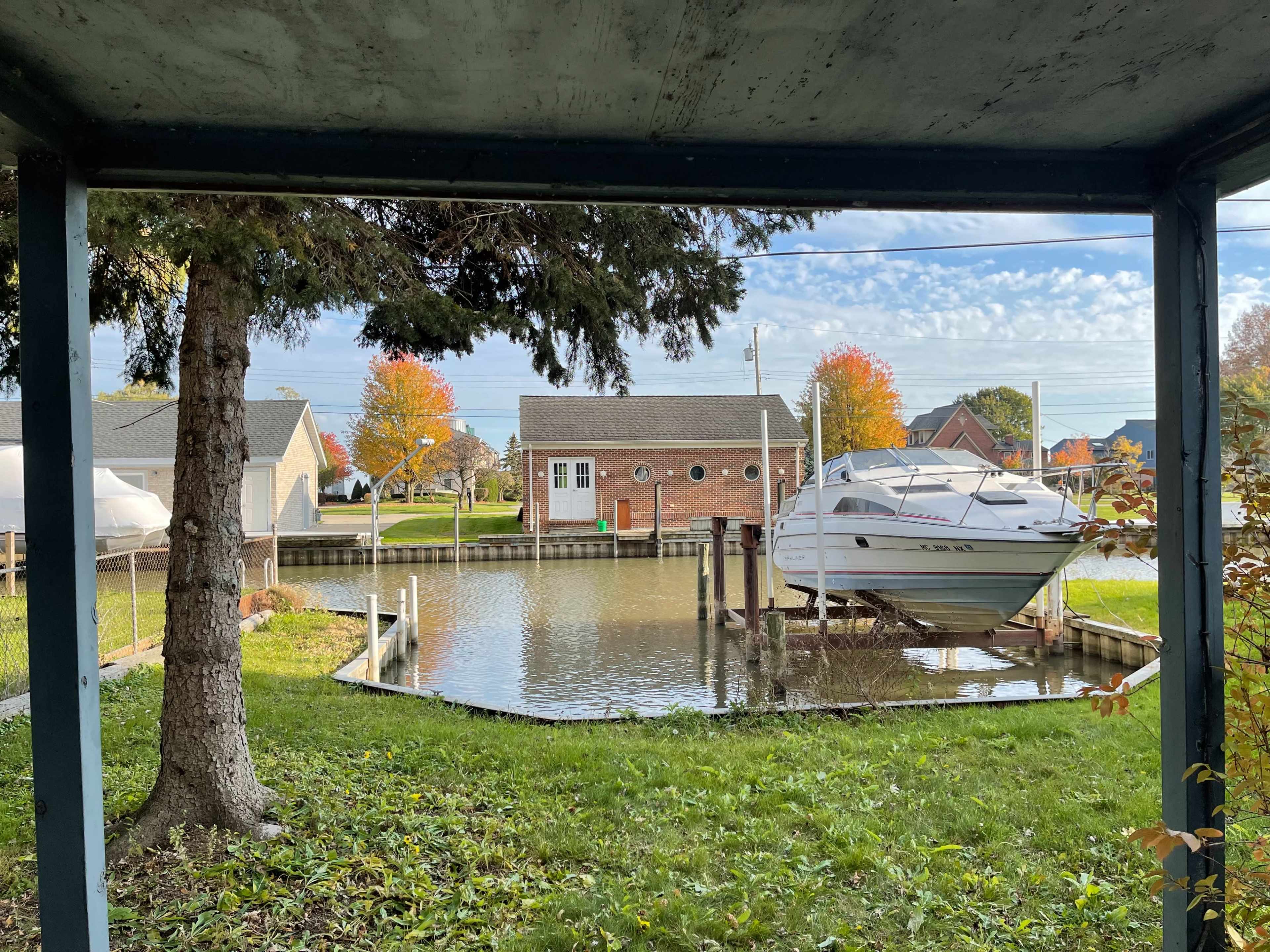 A boat is docked in a waterway next to a residential house, surrounded by trees and autumn-colored foliage.