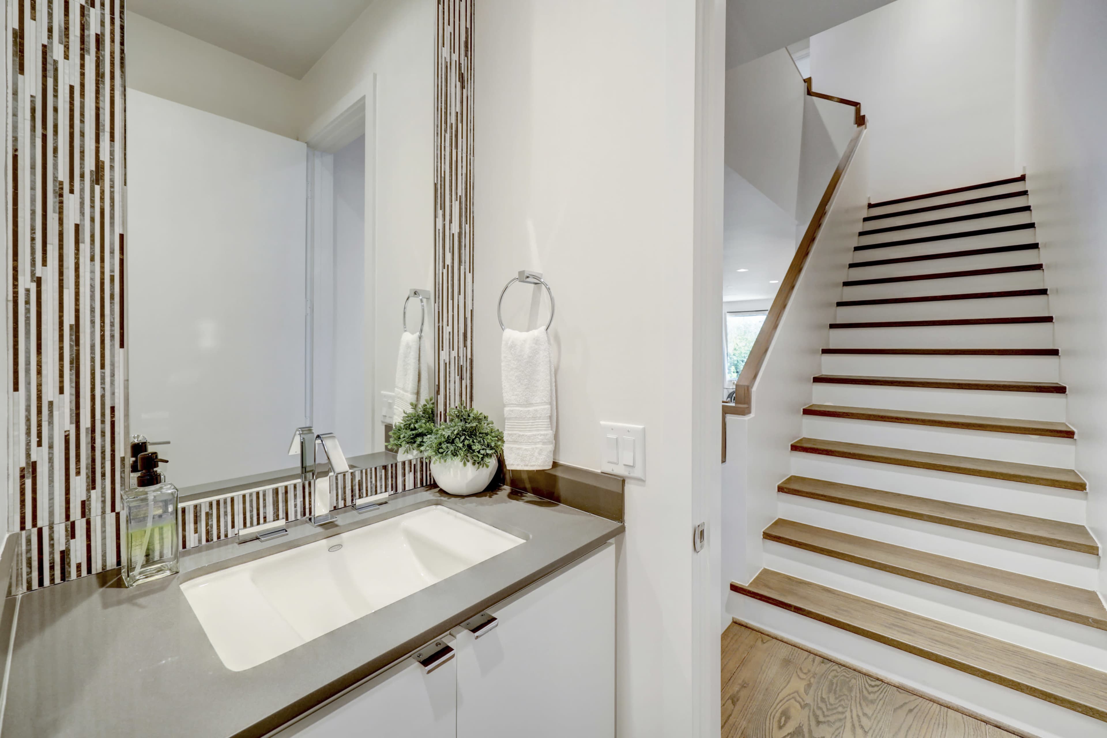 A modern bathroom with a double sink vanity and a staircase leading upwards in the background.