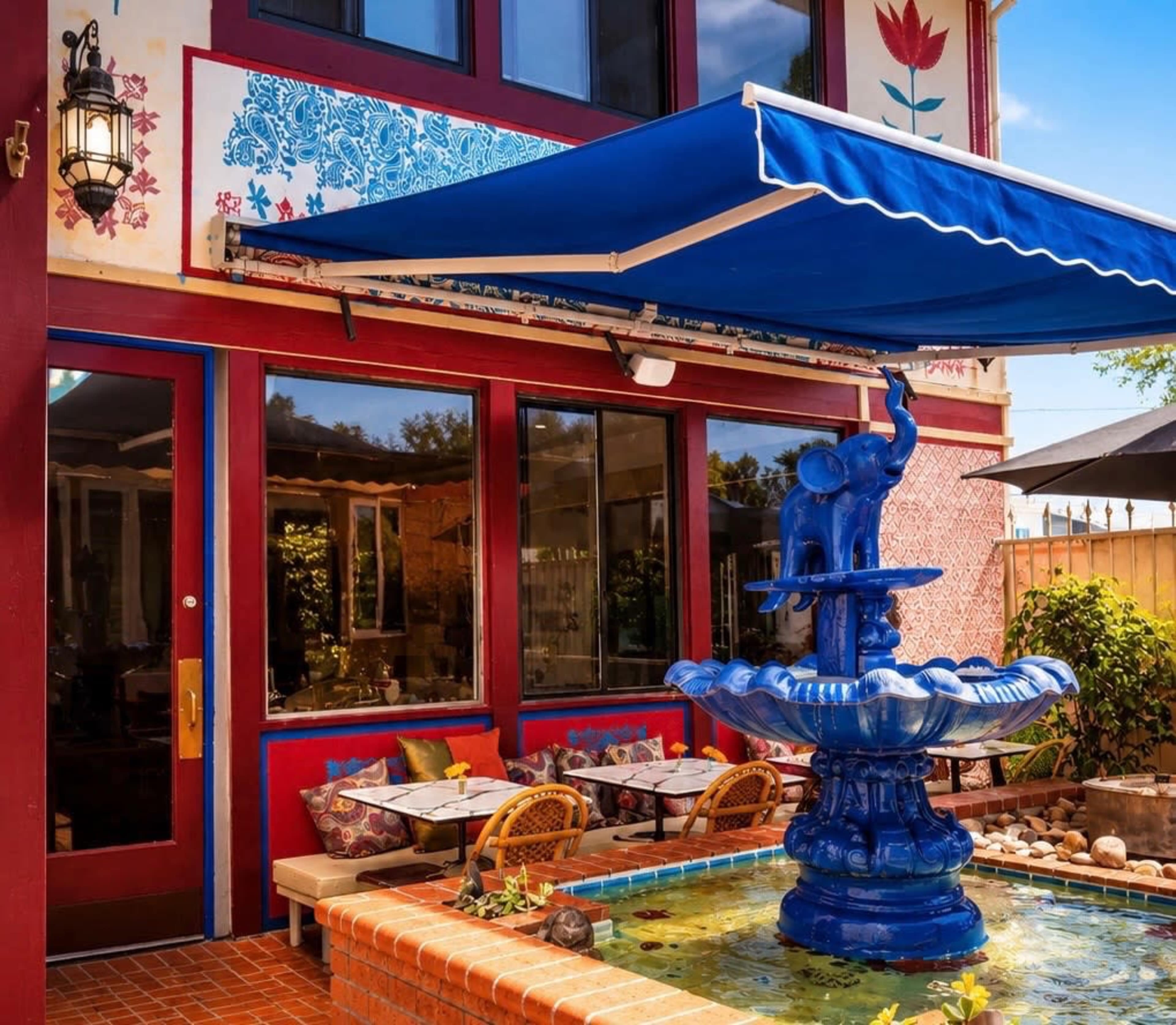 The image shows a colorful outdoor dining area with a blue fountain and tables under an awning.