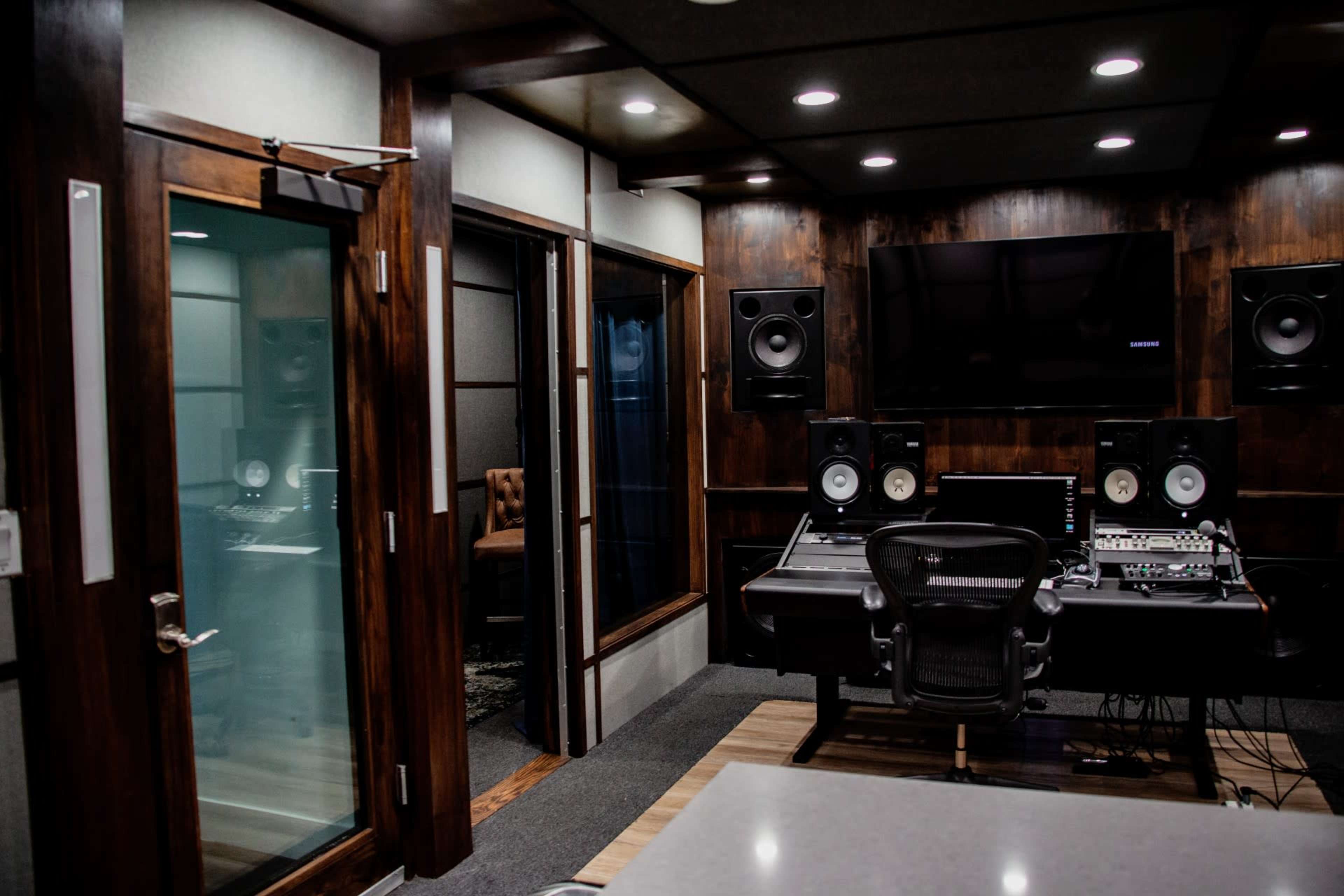 A professional recording studio with a control desk, speakers, and soundproof glass rooms.