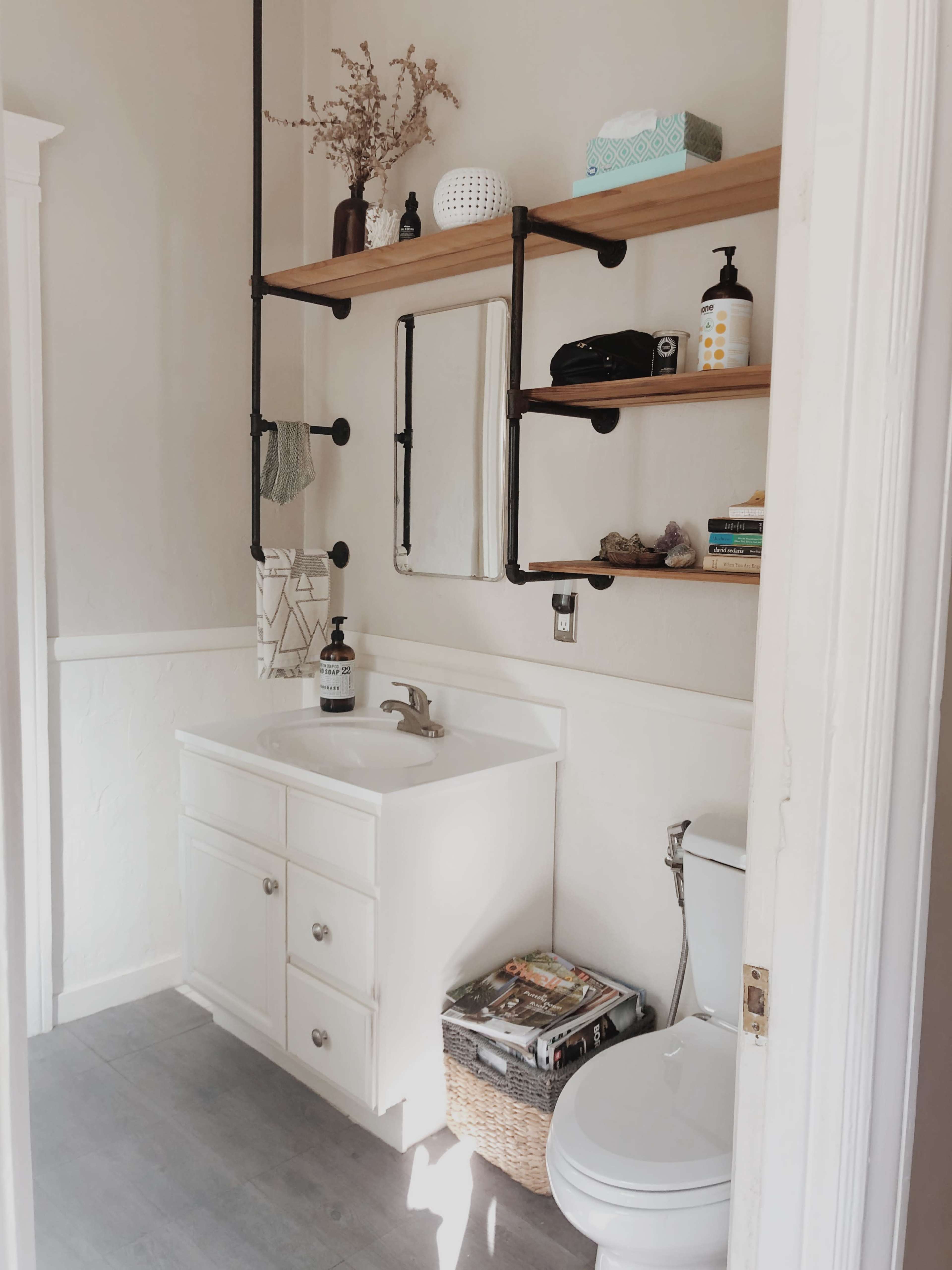 A bathroom with a white vanity, a toilet, and open shelves displaying various items above a sink.
