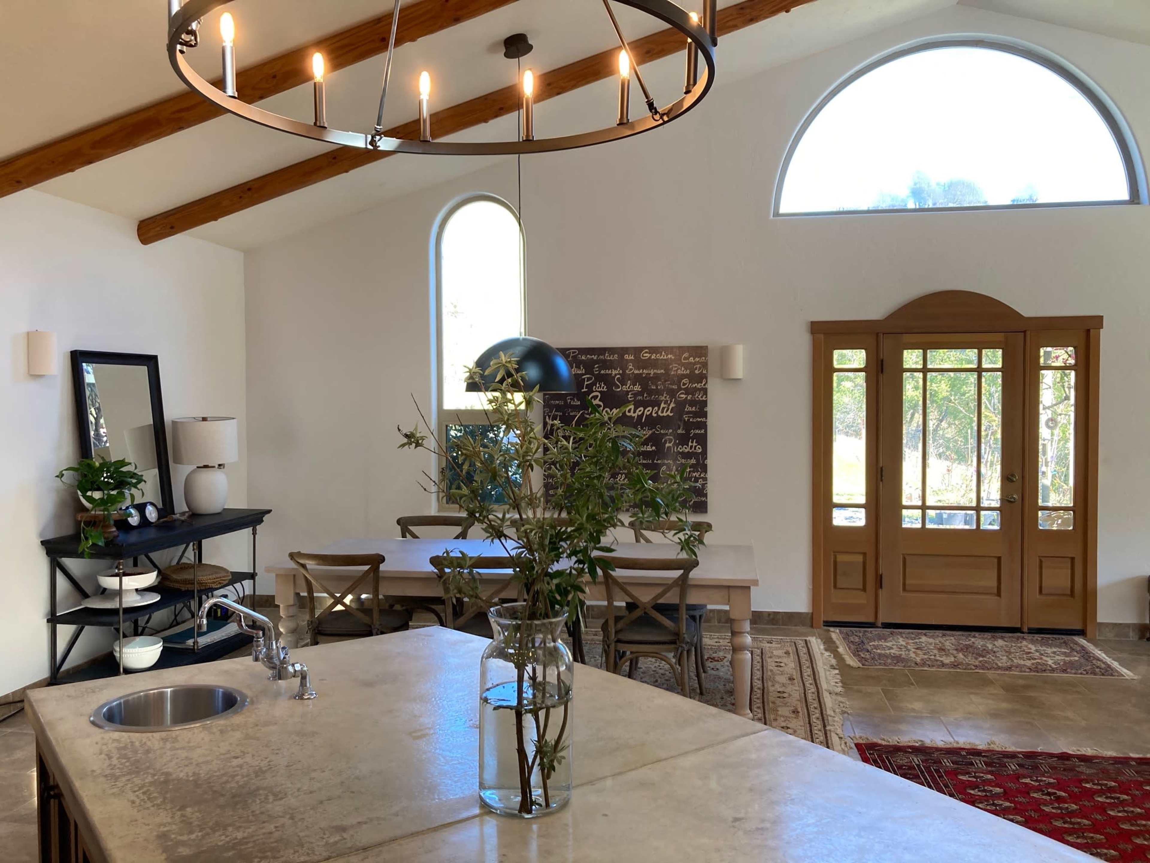 A spacious kitchen and dining area featuring a large island with a sink, a wooden dining table, and a front door with large windows.