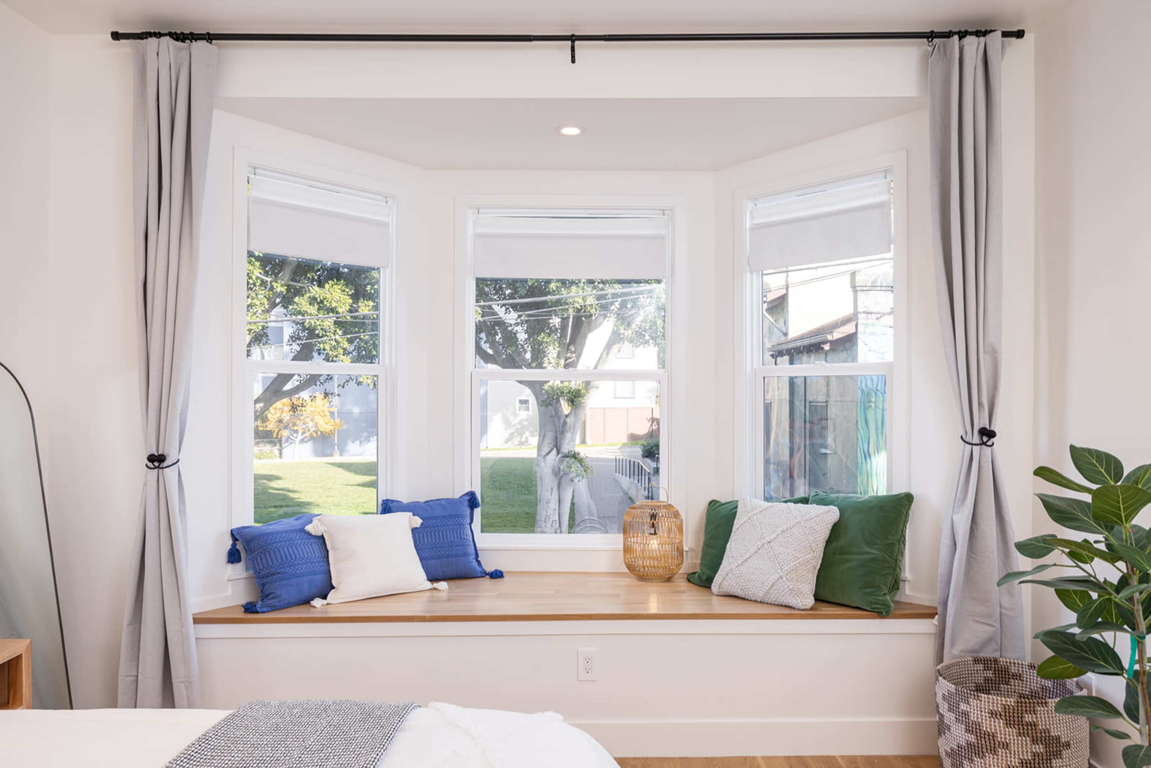 A bright bedroom features a bay window with a wooden ledge, adorned with cushions and natural light streaming in.