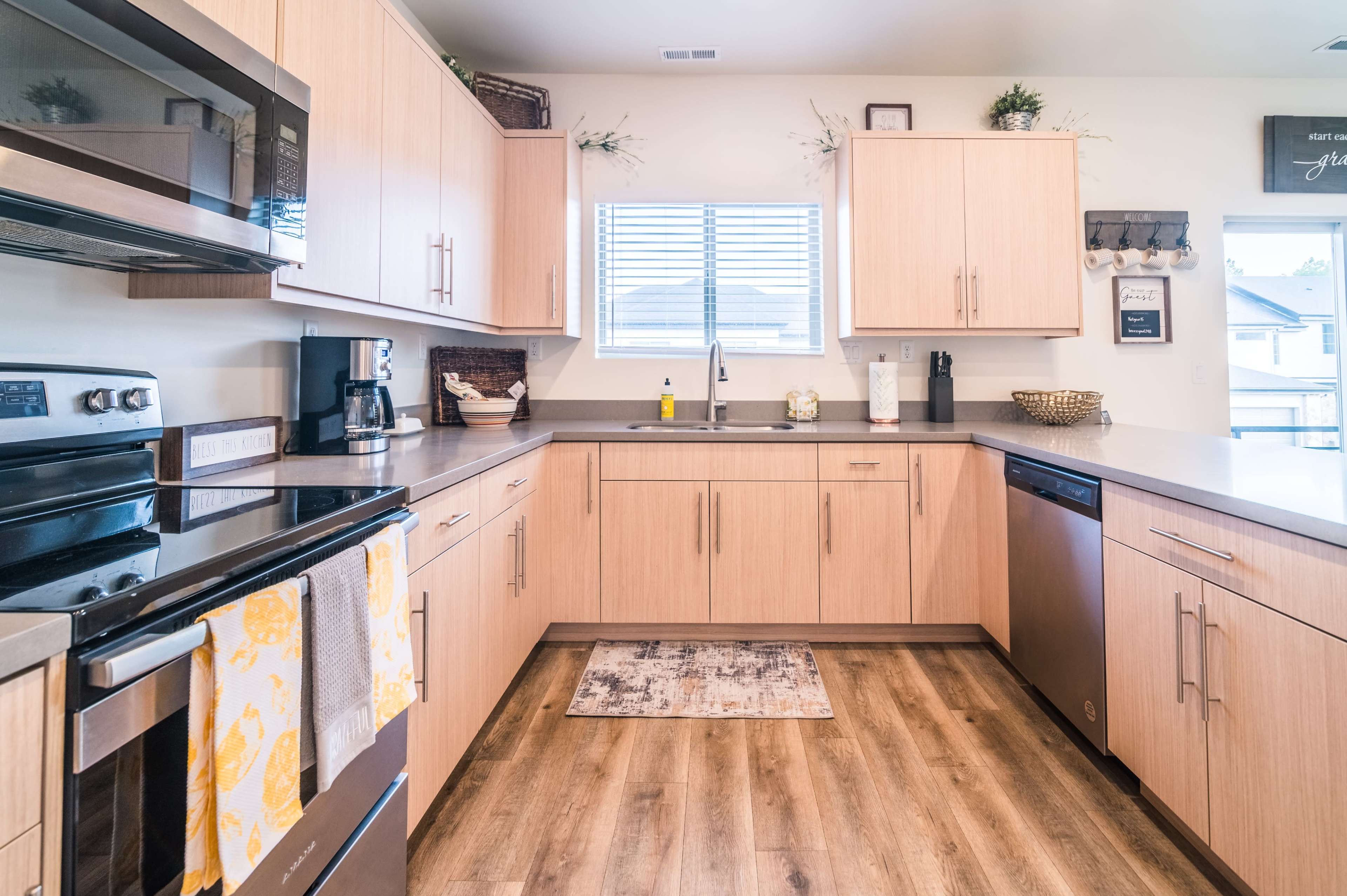 A modern kitchen features light wooden cabinetry, stainless steel appliances, and a window providing natural light.