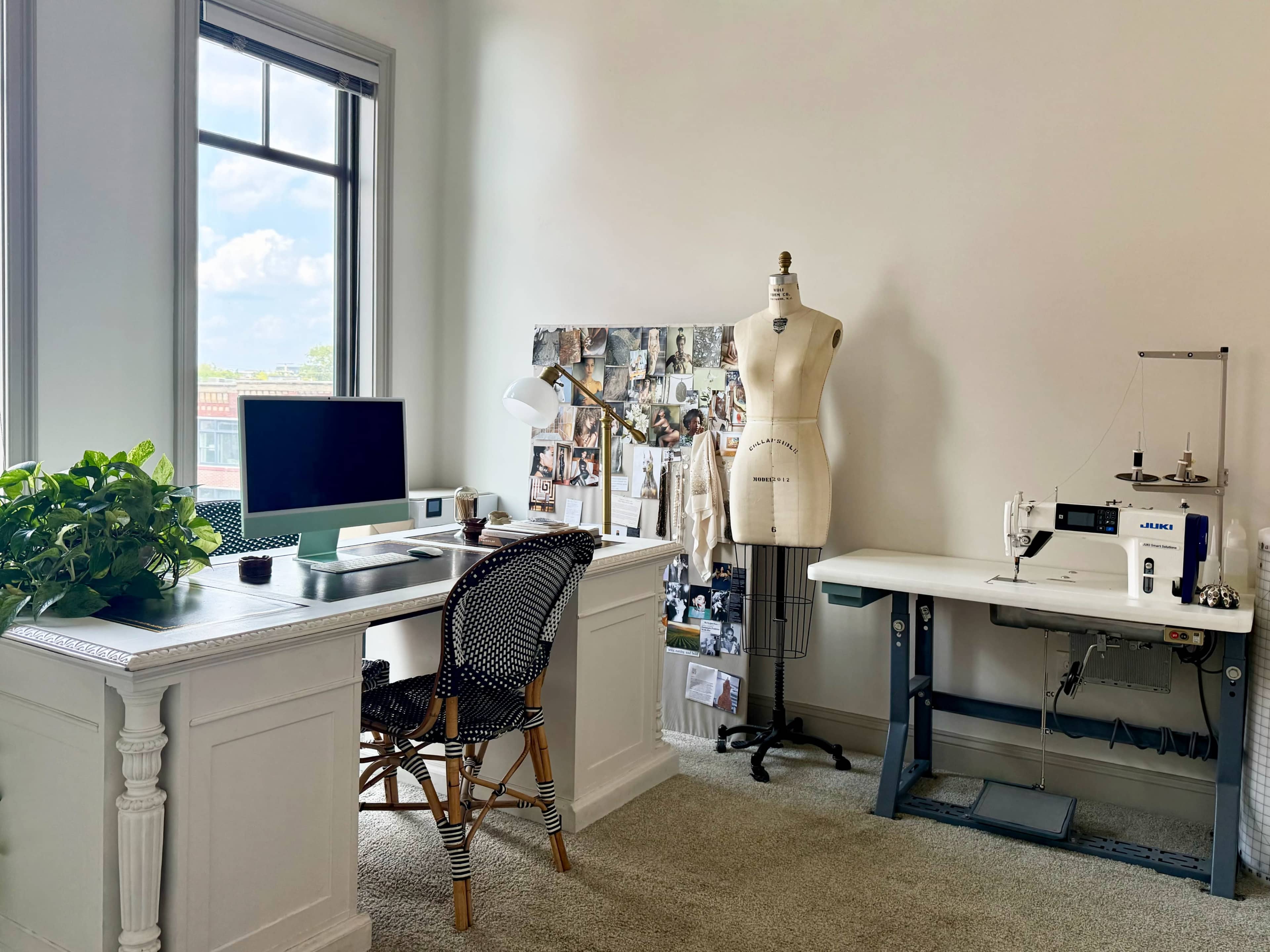 The image shows a contemporary workspace featuring a desk with a computer, a dressmaker's mannequin, a bulletin board with images, and a sewing machine.