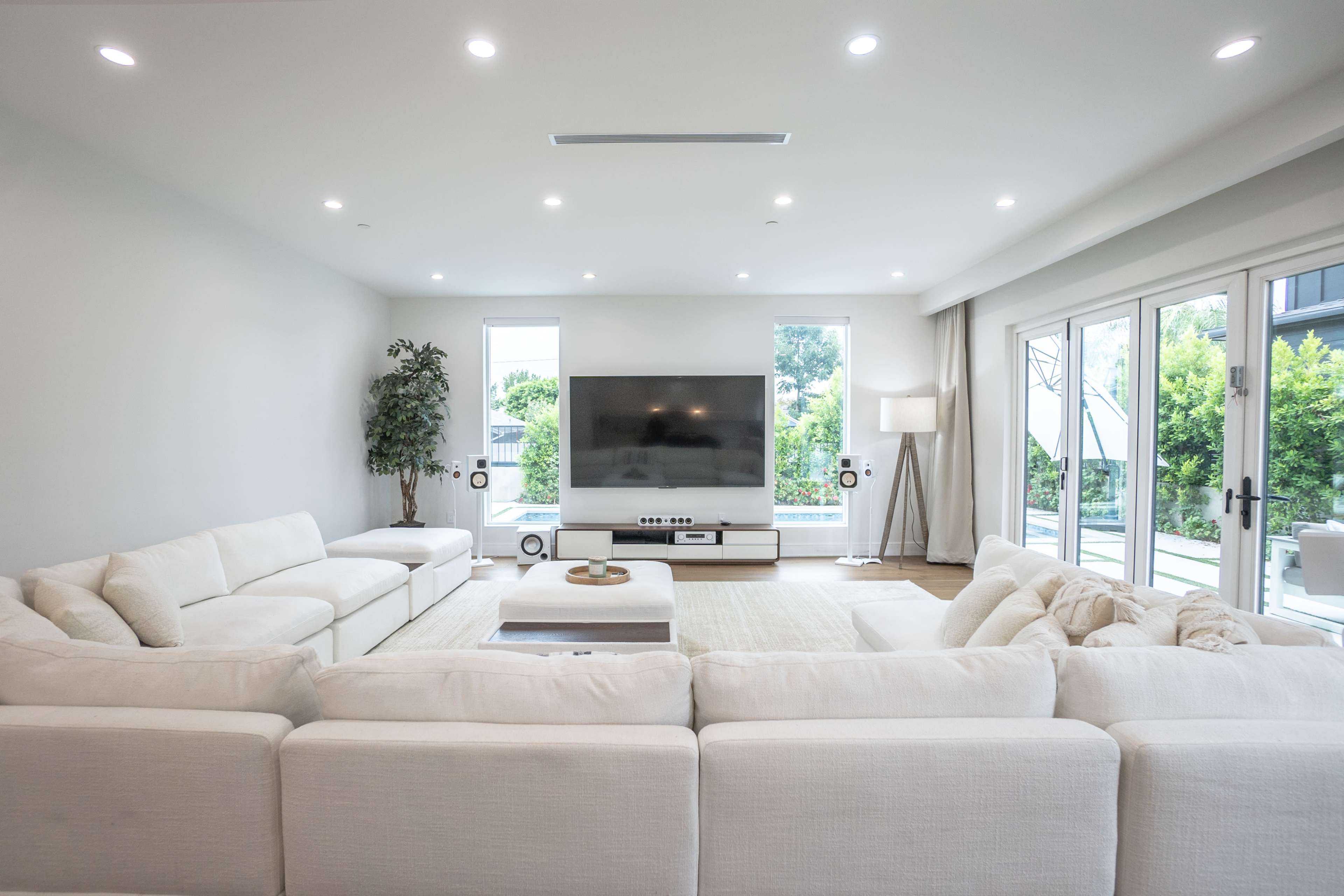 A modern living room features a large sectional sofa, a flat-screen television, and glass doors leading to an outdoor space.
